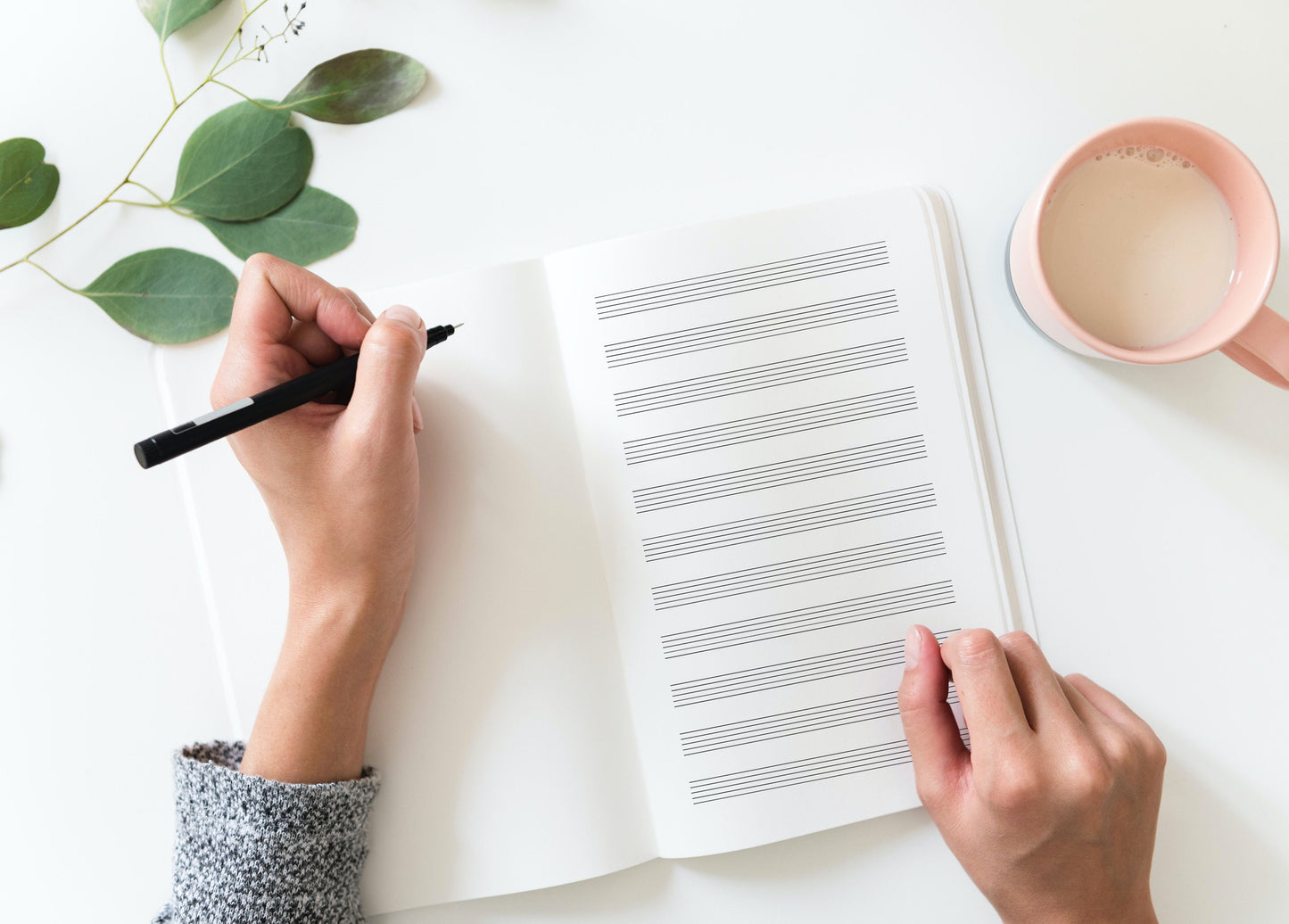 Blank staff paper in notebook on white desk in front of woman holding pen