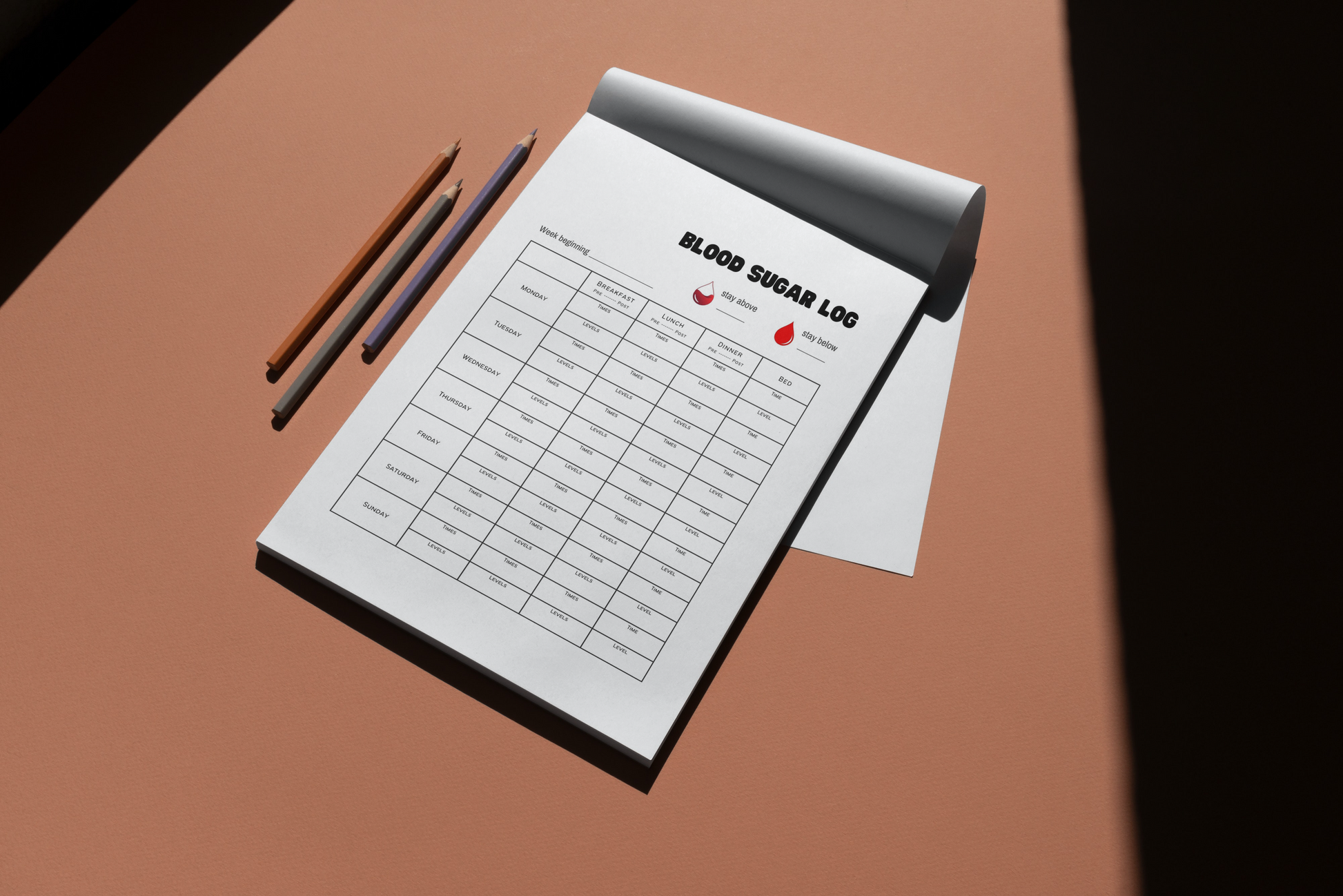Printable daily blood sugar log in notebook on desk beside pencils