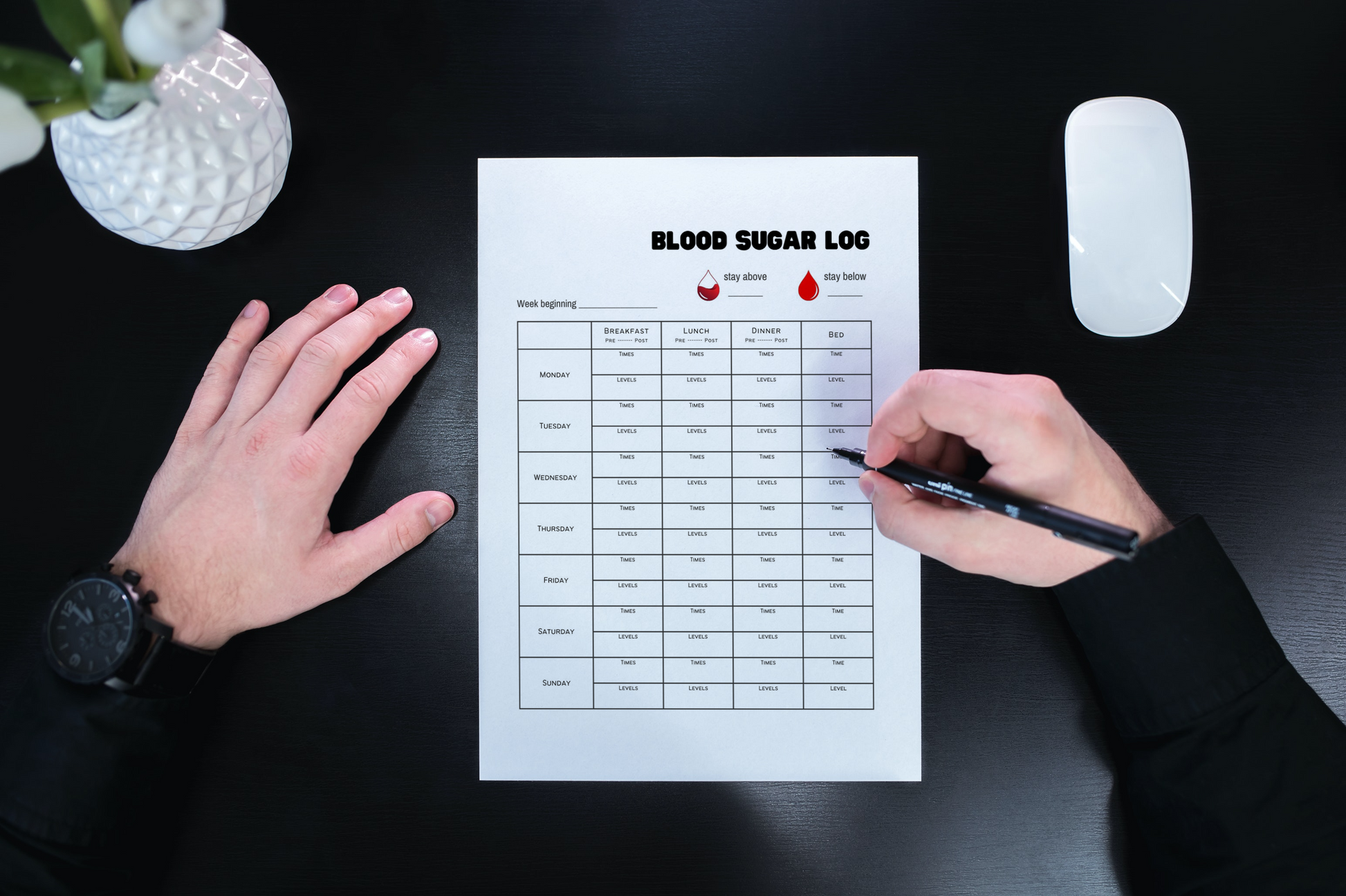 Printable glucose tracker on black desk in front of a man holding a pen