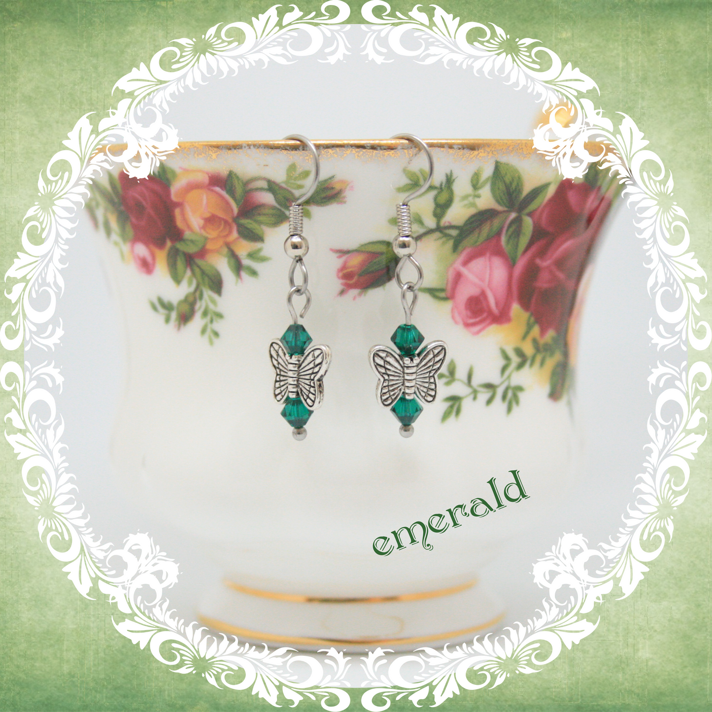 Handmade silver butterfly earrings with emerald green crystal beads shown on floral china teacup