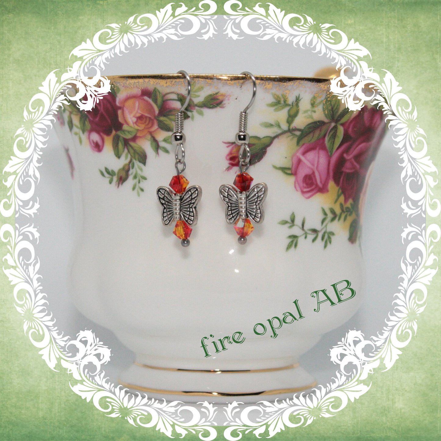 Handmade silver butterfly earrings with orange red crystal beads shown on floral china teacup
