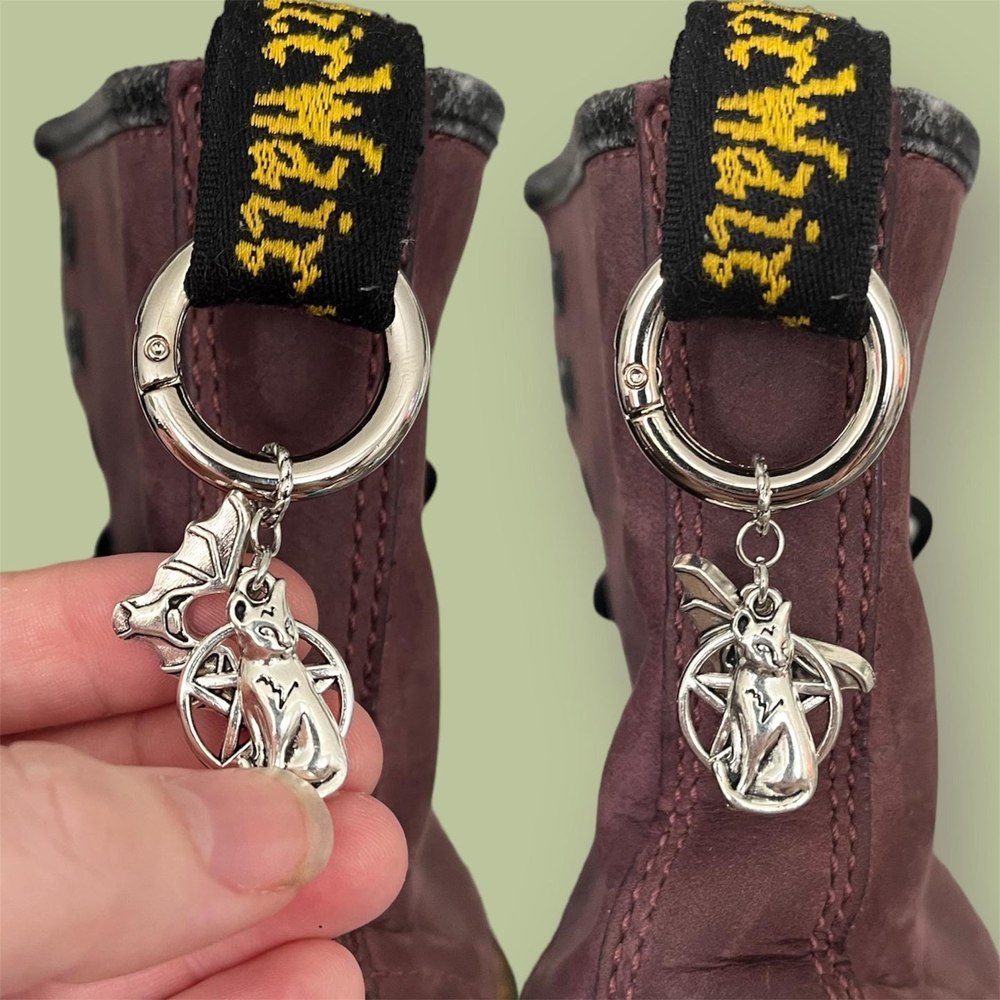 Close-up of handmade silver boot charms with cat, pentagram, and bat designs clipped onto black boot tabs