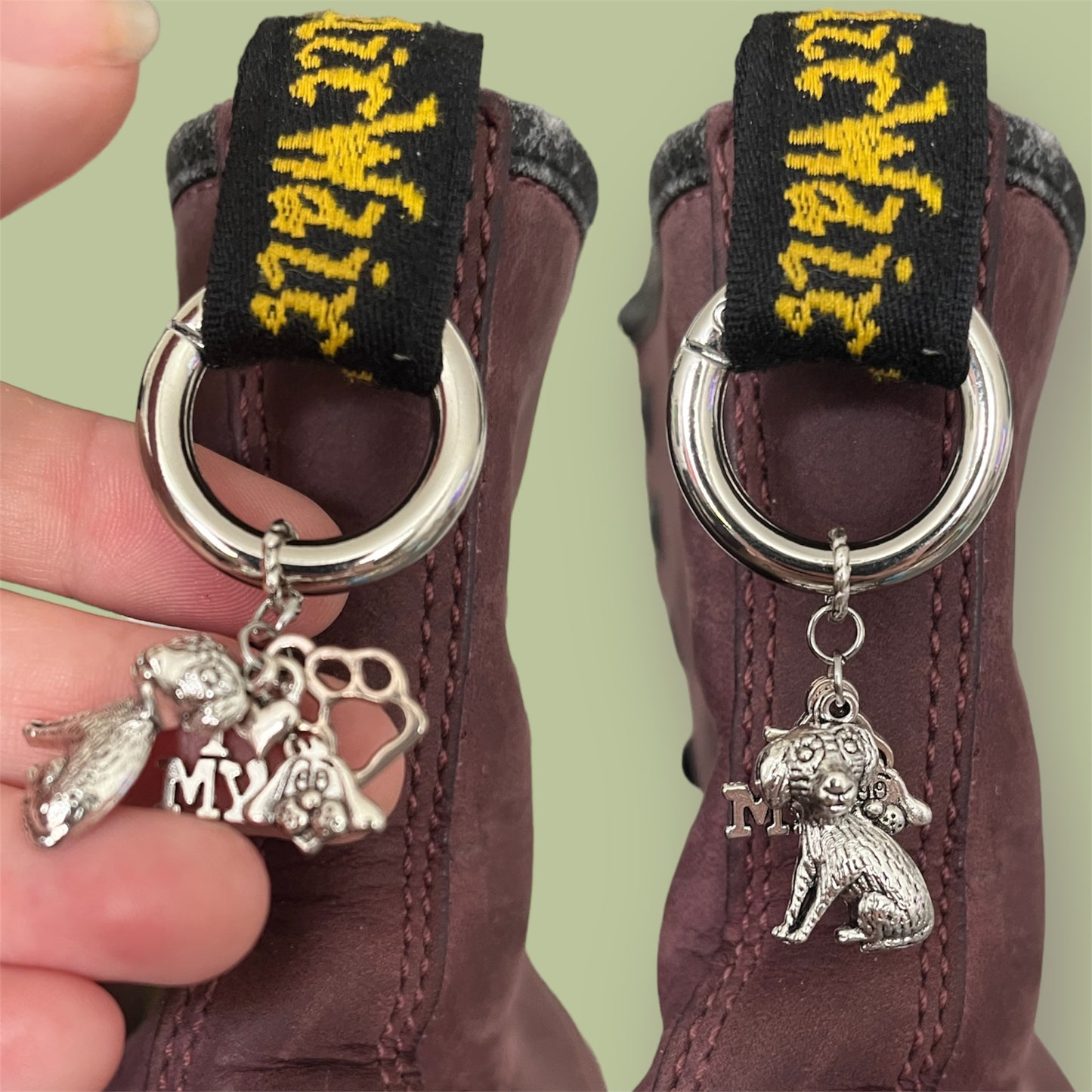 Close-up of handmade silver boot charms with sitting dog, the words I heart my dog, and paw print designs clipped onto black boot tabs