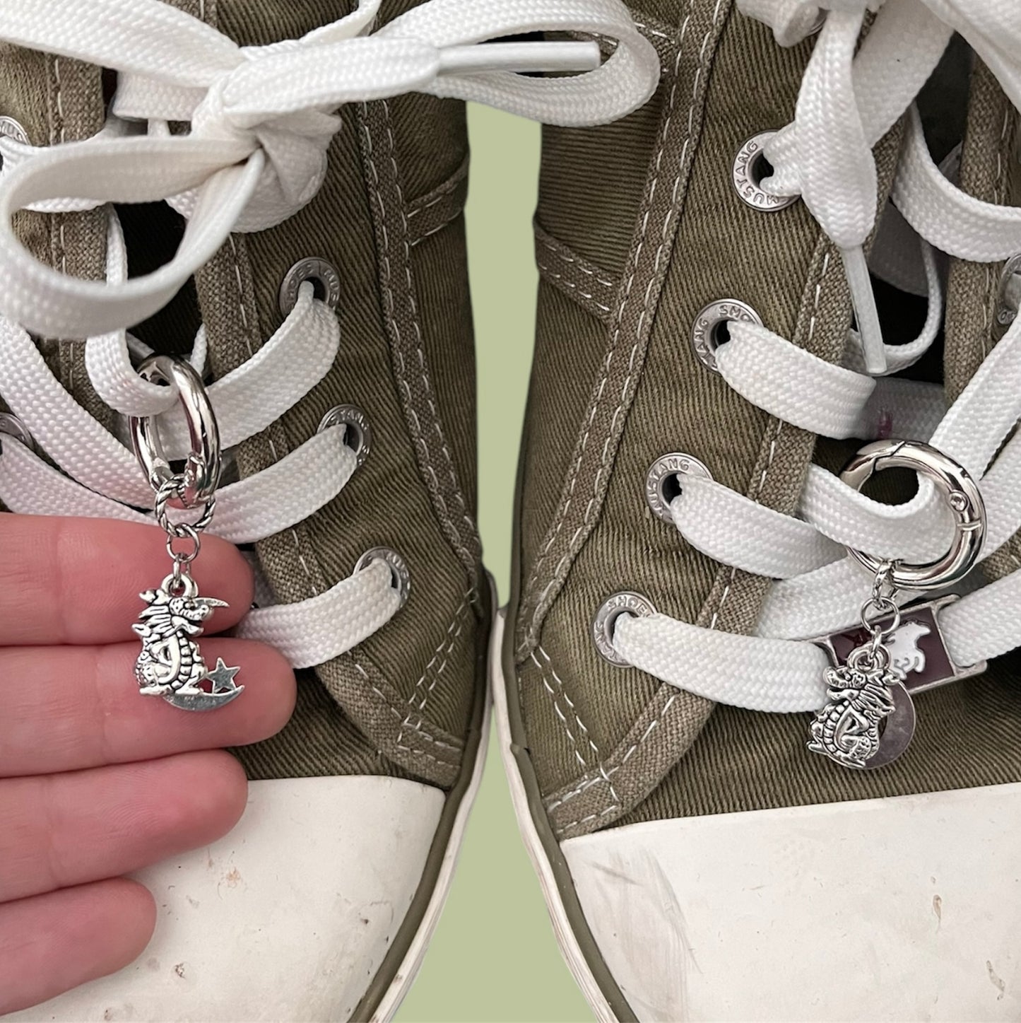 Close-up of handmade silver lace charms with dragon, moon and star designs clipped onto white shoelaces