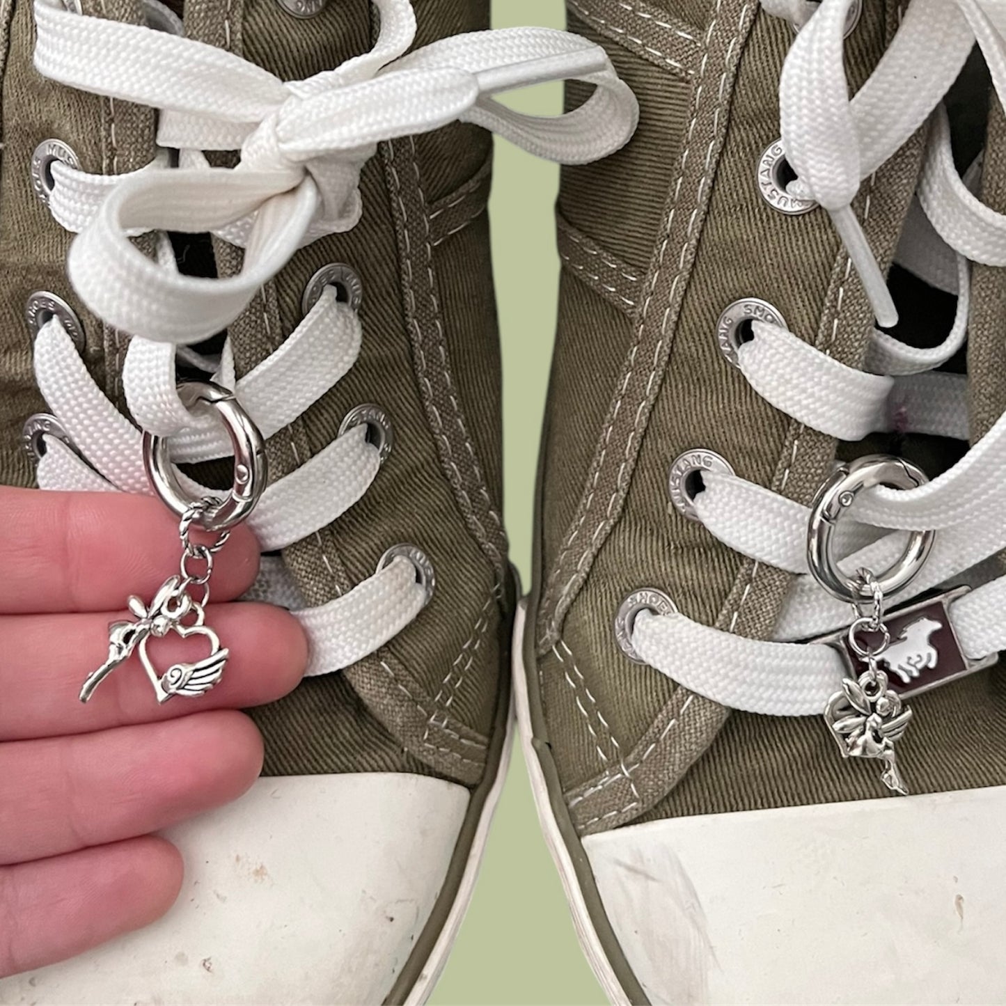Close-up of handmade silver lace charms with fairy and heart with wing designs clipped onto white shoelaces