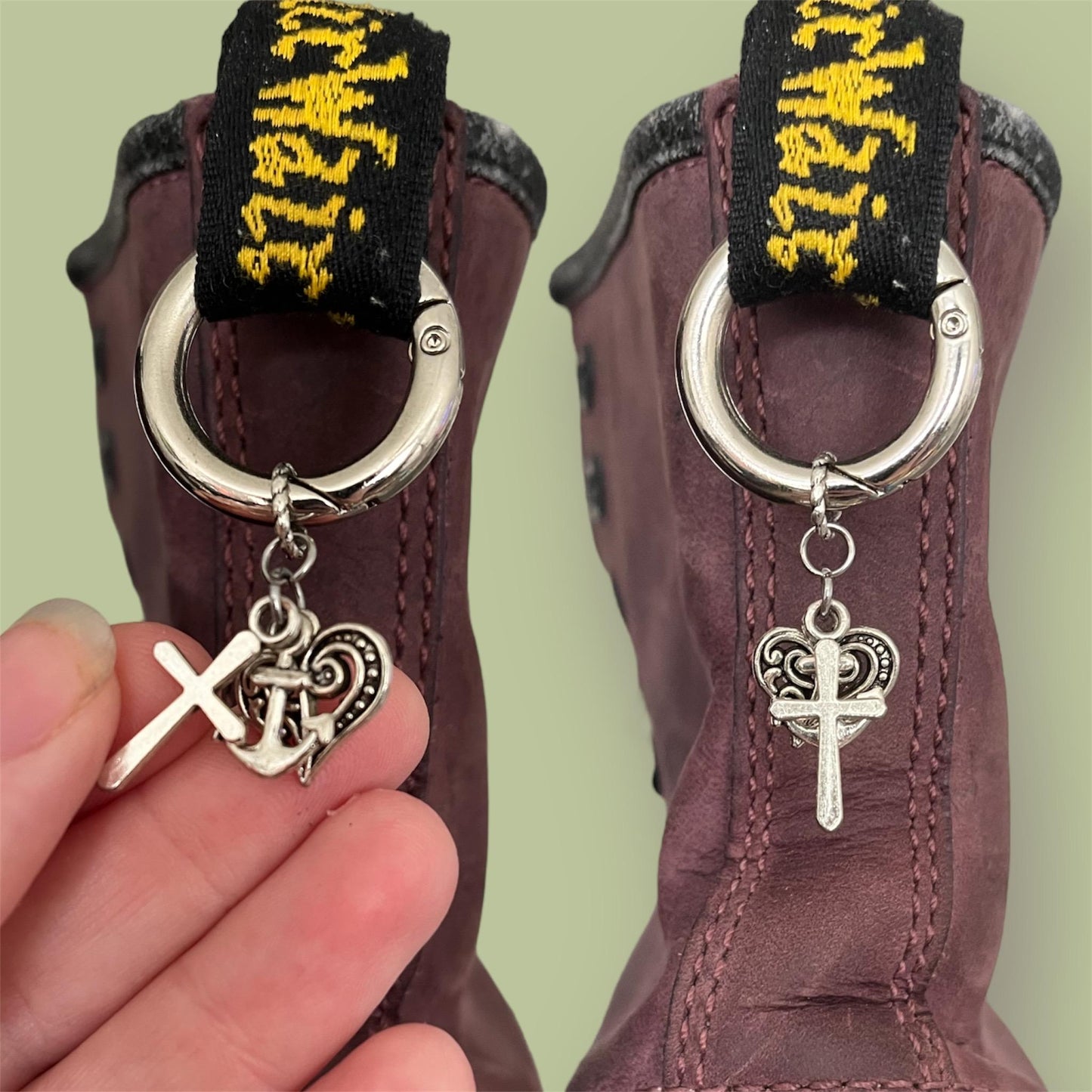 Close-up of handmade silver boot charms with cross, anchor, and heart designs clipped onto black boot tabs