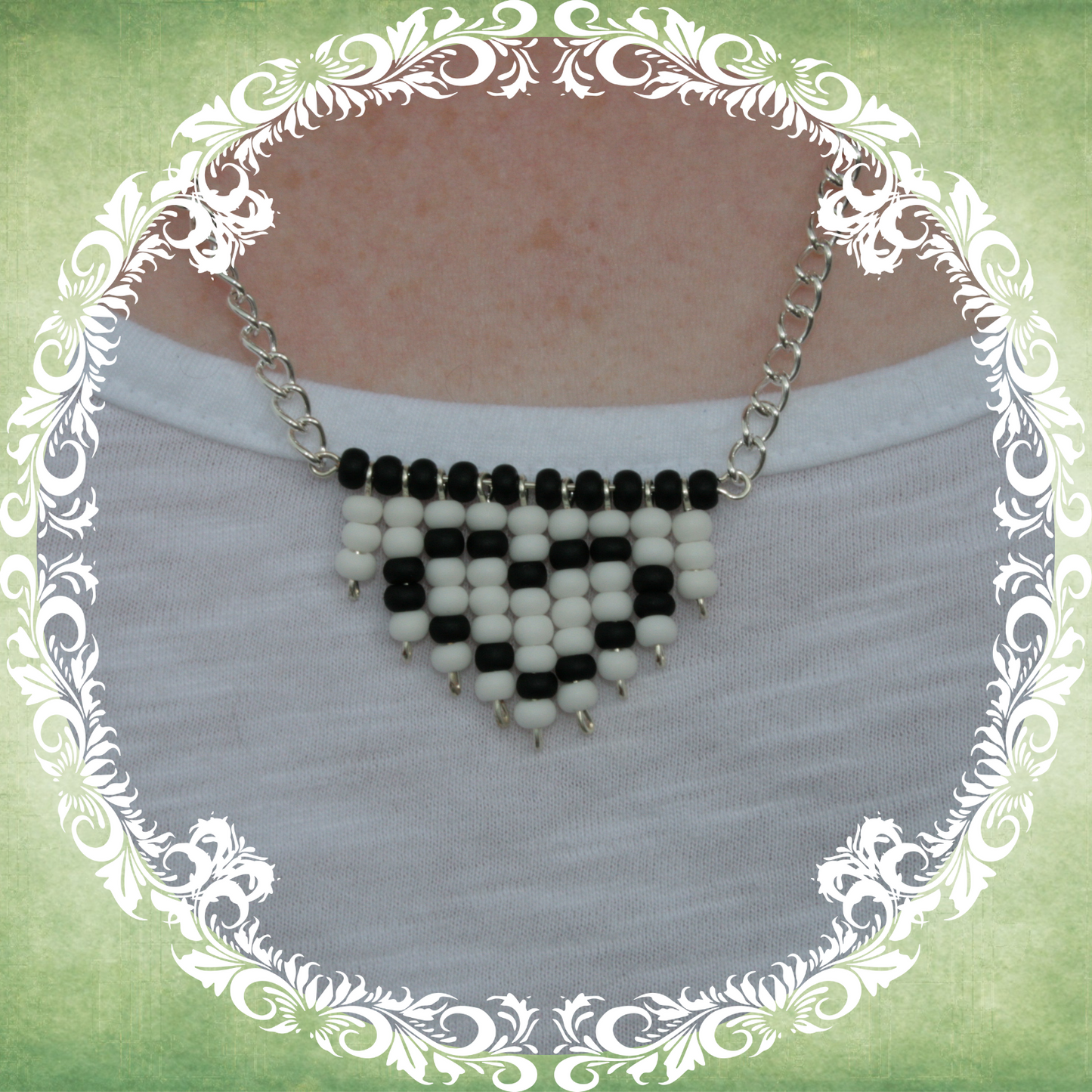 Handmade white and black heart fringe necklace with bold beadwork and playful fringe design, featuring a silver-plated chain, pictured on white t-shirt.