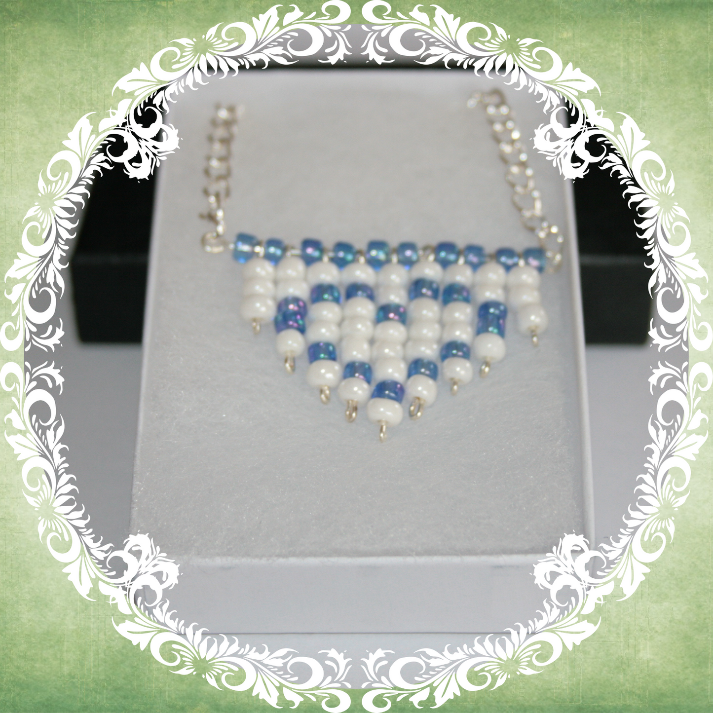 Handmade white and blue heart fringe necklace with bold beadwork and playful fringe design, featuring a silver-plated chain, pictured in a white box.
