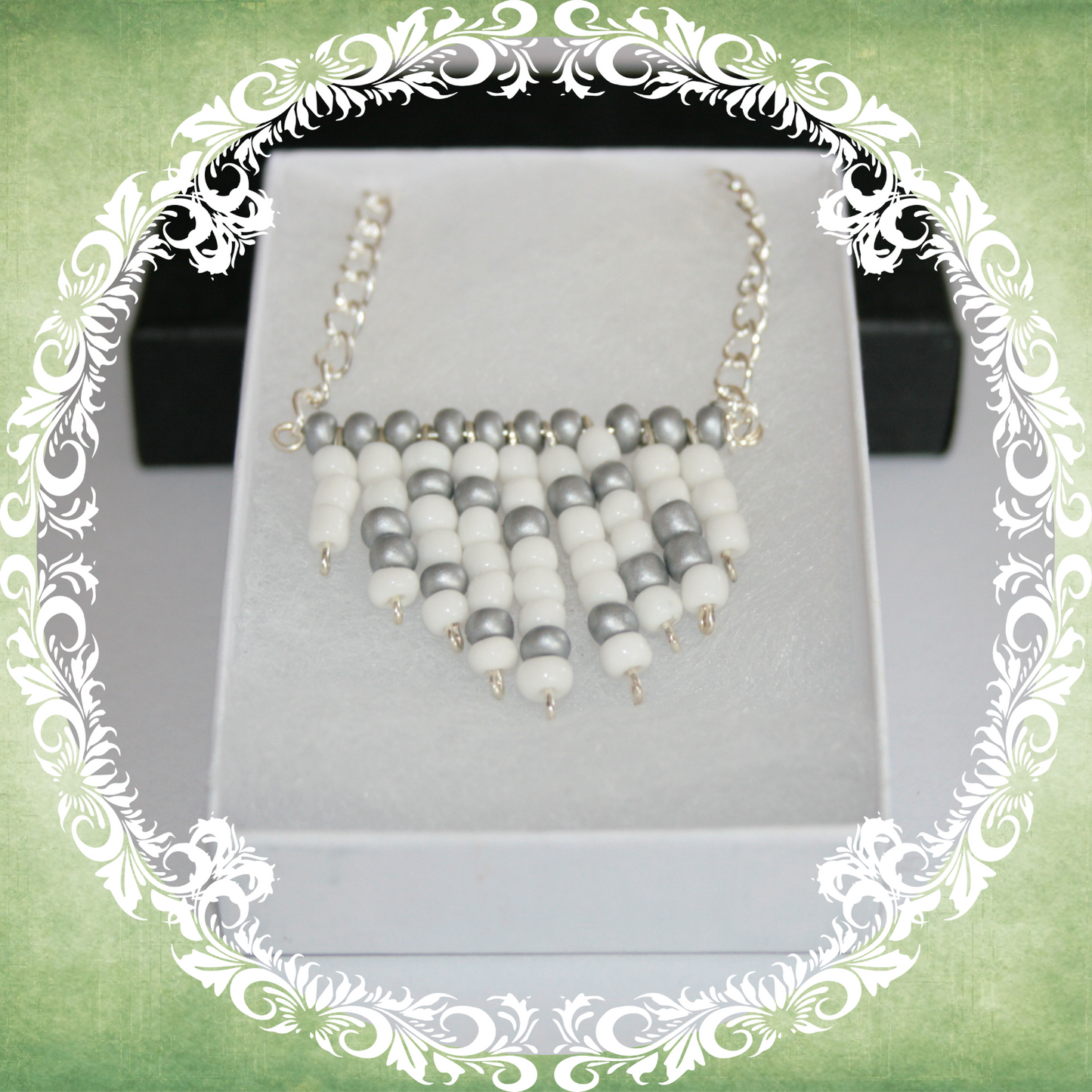Handmade white and silver heart fringe necklace with bold beadwork and playful fringe design, featuring a silver-plated chain, pictured in a white box.