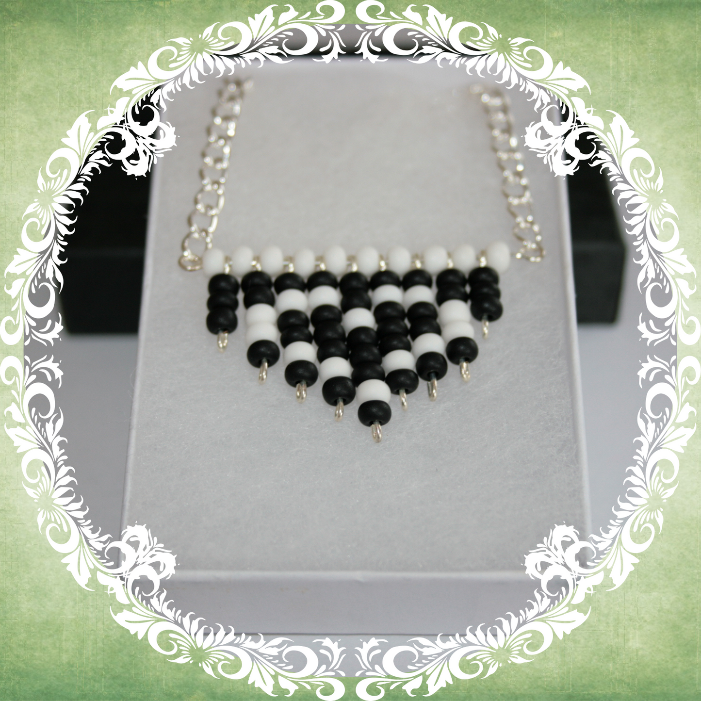 Handmade black and white heart fringe necklace with bold beadwork and playful fringe design, featuring a silver-plated chain, pictured in a white box.