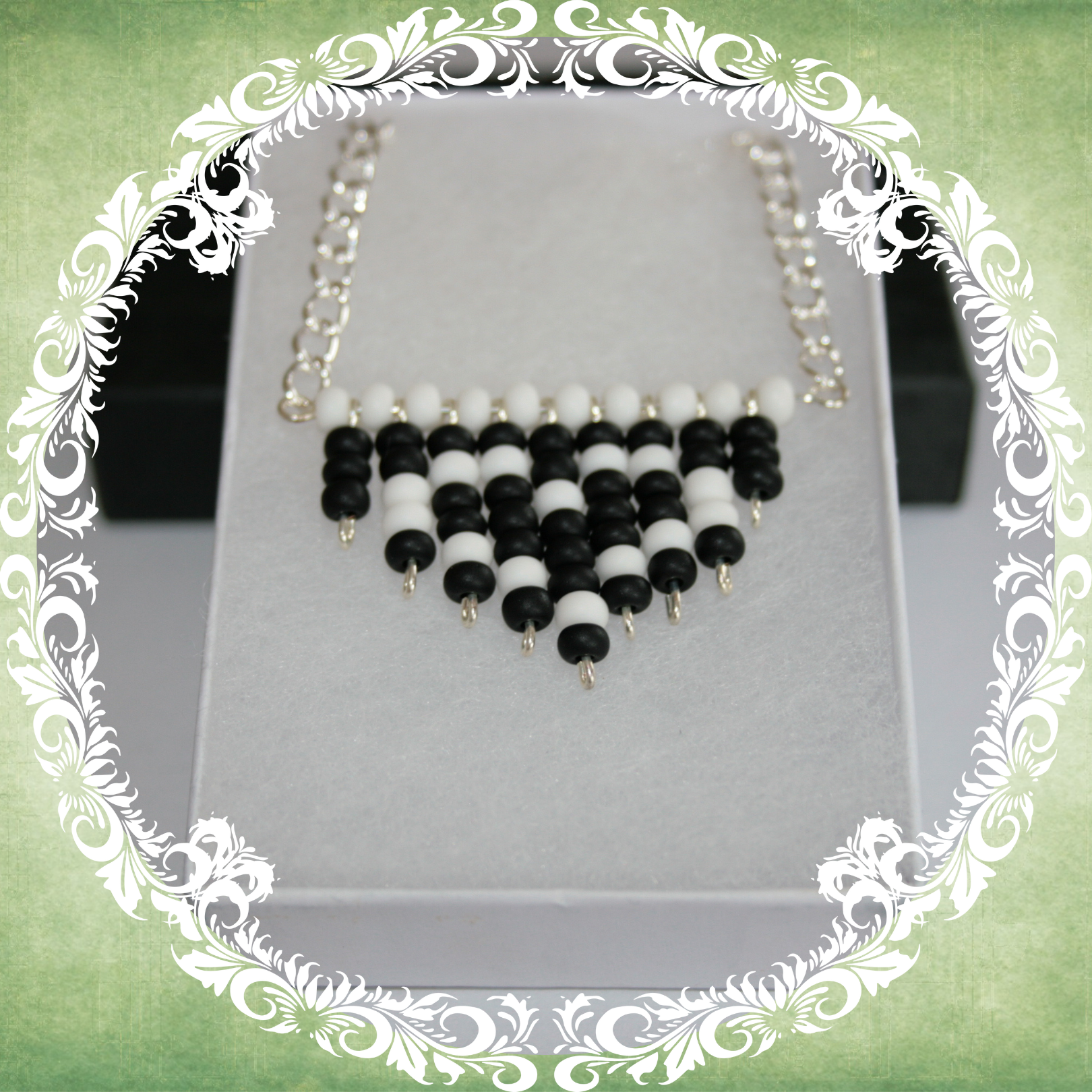 Handmade black and white heart fringe necklace with bold beadwork and playful fringe design, featuring a silver-plated chain, pictured in a white box.