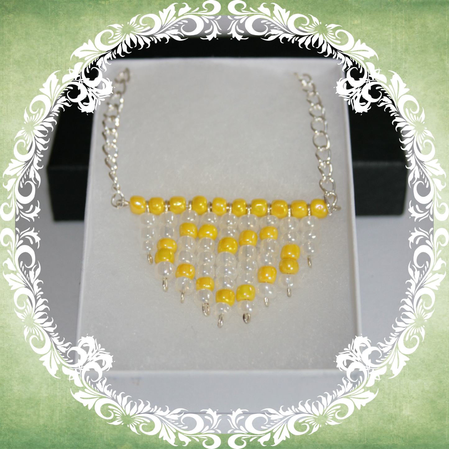 Handmade white and yellow heart fringe necklace with bold beadwork and playful fringe design, featuring a silver-plated chain, pictured in a white box.