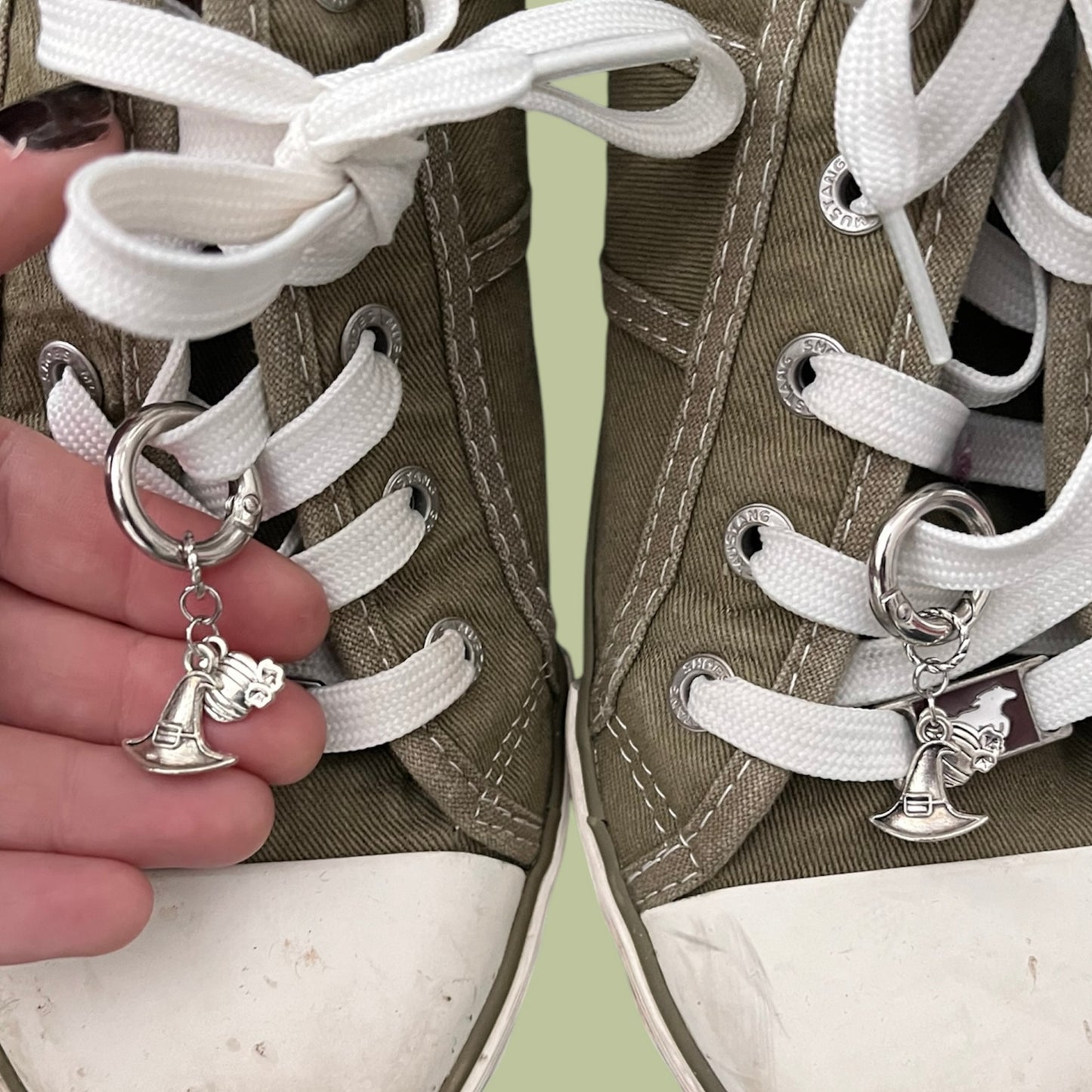 Close-up of handmade silver lace charms with witch's hat and pumpkin designs clipped onto white shoelaces