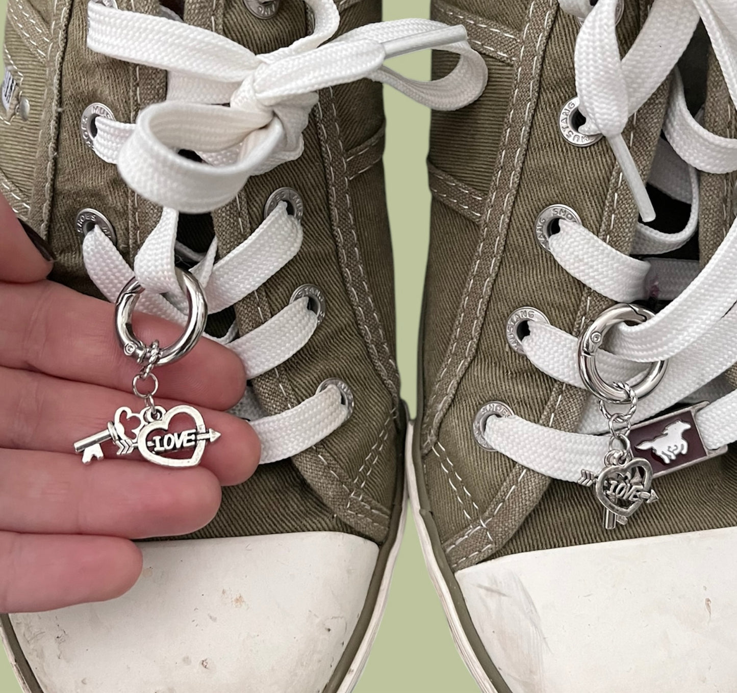 Close-up of handmade silver lace charms with key and open heart with the word love and an arrow designs clipped onto white shoelaces