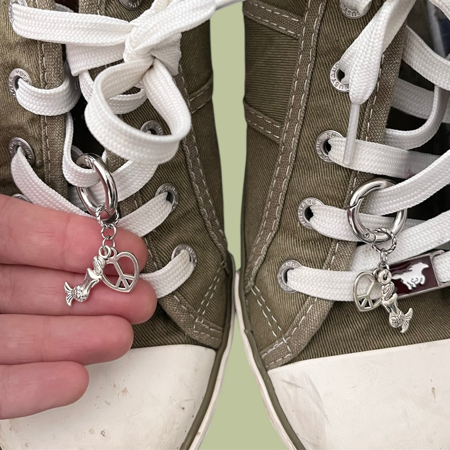 Close-up of handmade silver lace charms with mermaid and open heart with peace sign designs clipped onto white shoelaces