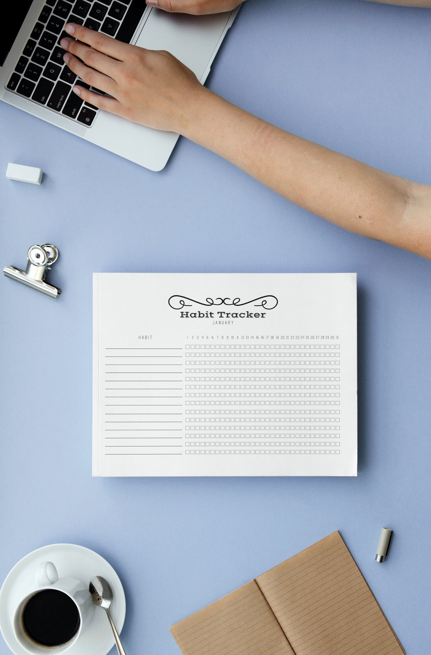 Printable habit tracker on blue desk next to person with laptop