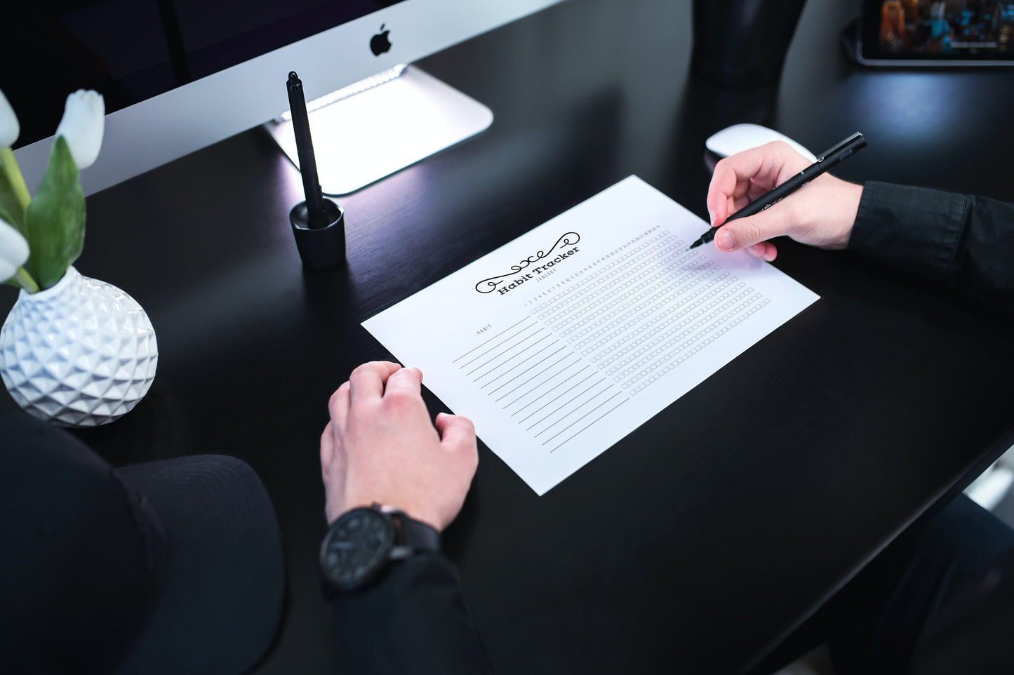 Printable habit tracker on black desk in front of a man holding a pen
