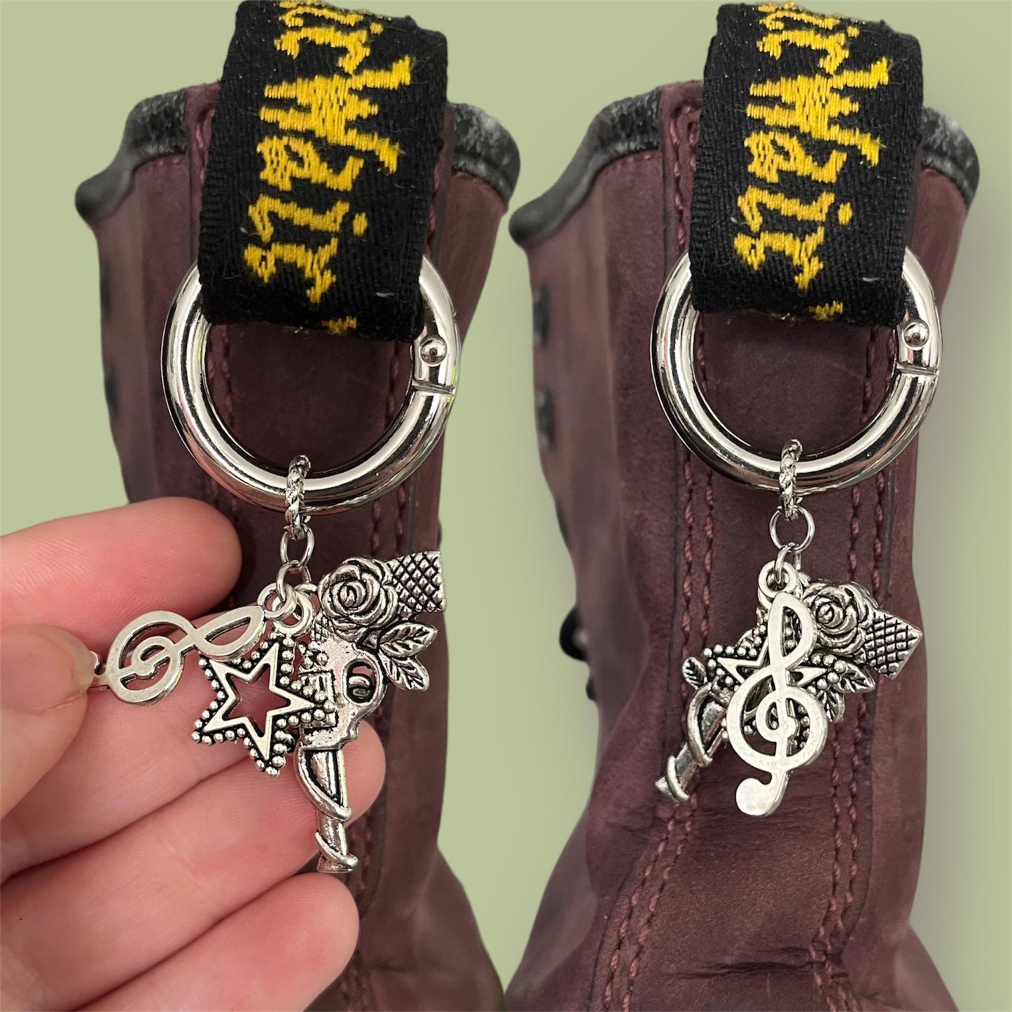 Close-up of handmade silver boot charms with treble clef, open star, and gun with rose designs clipped onto black boot tabs
