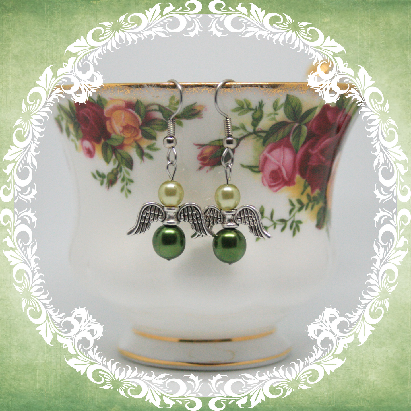 Handmade angel wing dangle earrings with two shades of green pearls on stainless steel ear wires shown on vintage floral teacup