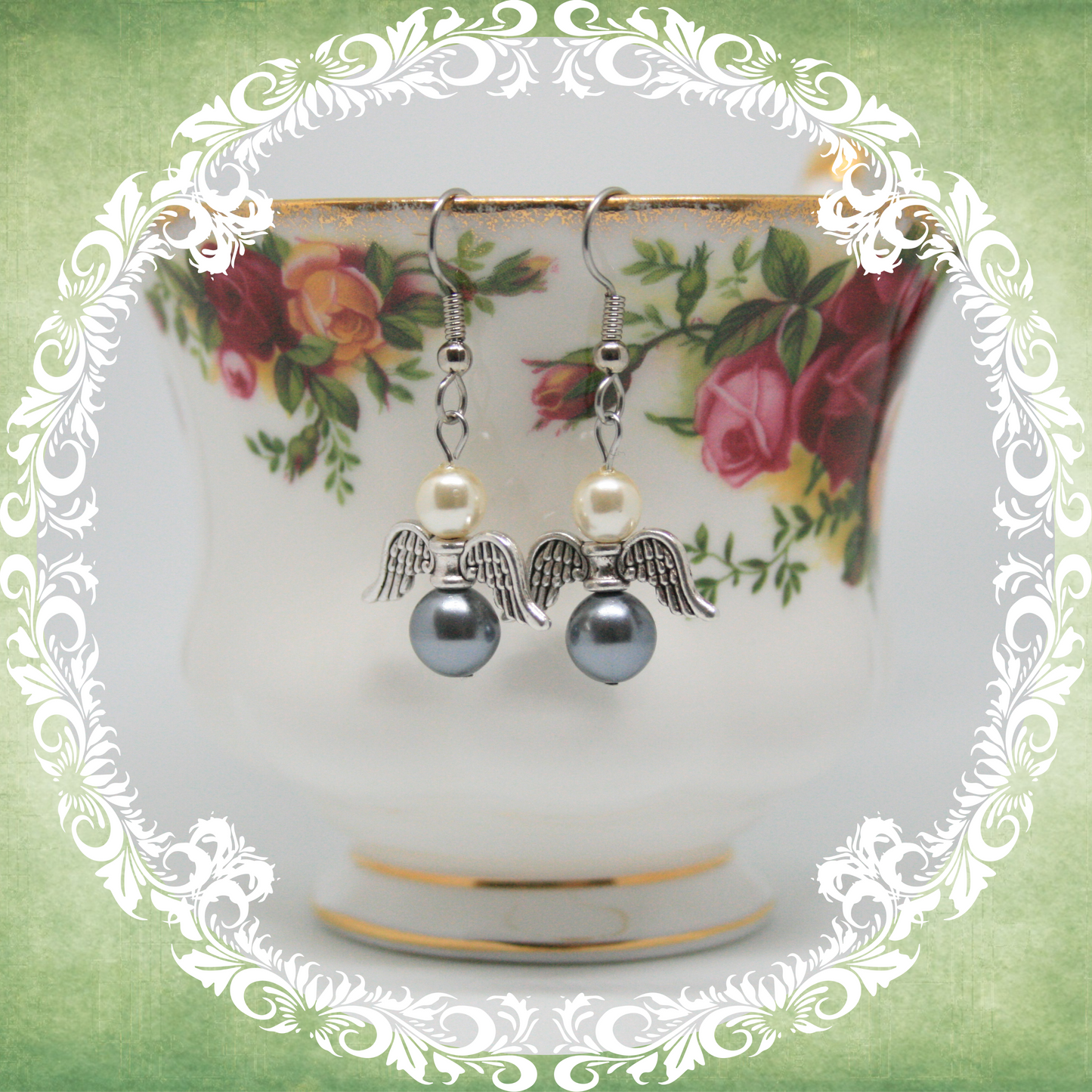 Handmade angel wing dangle earrings with white and grey pearls on stainless steel ear wires shown on vintage floral teacup