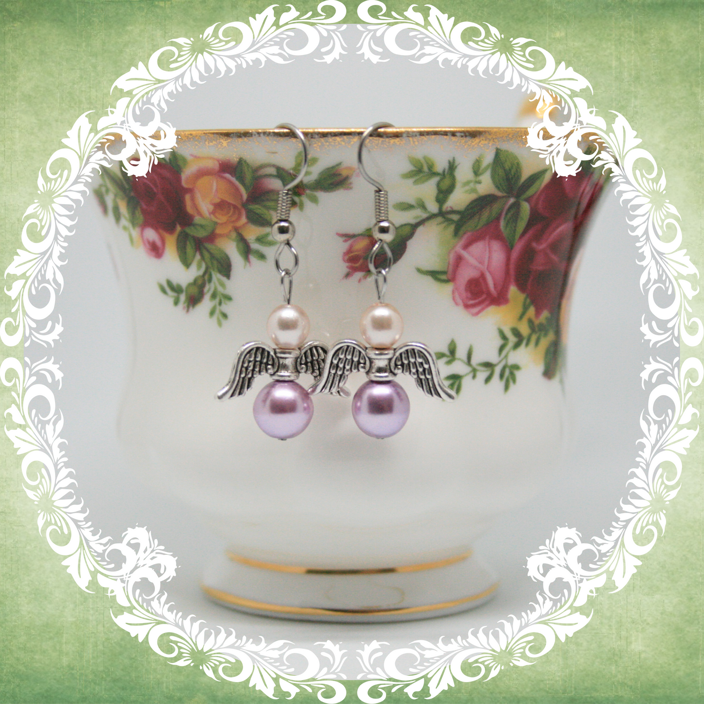 Handmade angel wing dangle earrings with pink and lilac pearls on stainless steel ear wires shown on vintage floral teacup