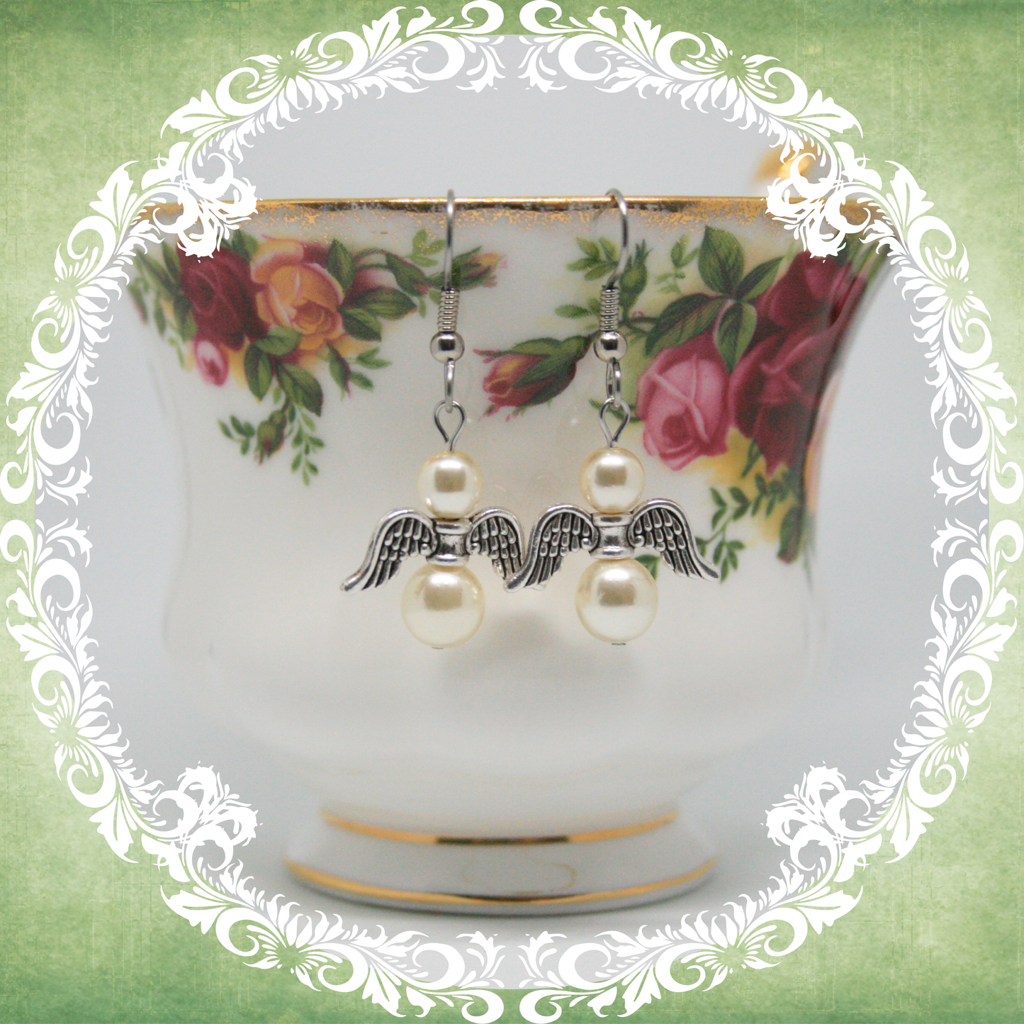 Handmade angel wing dangle earrings with white pearls on stainless steel ear wires shown on vintage floral teacup