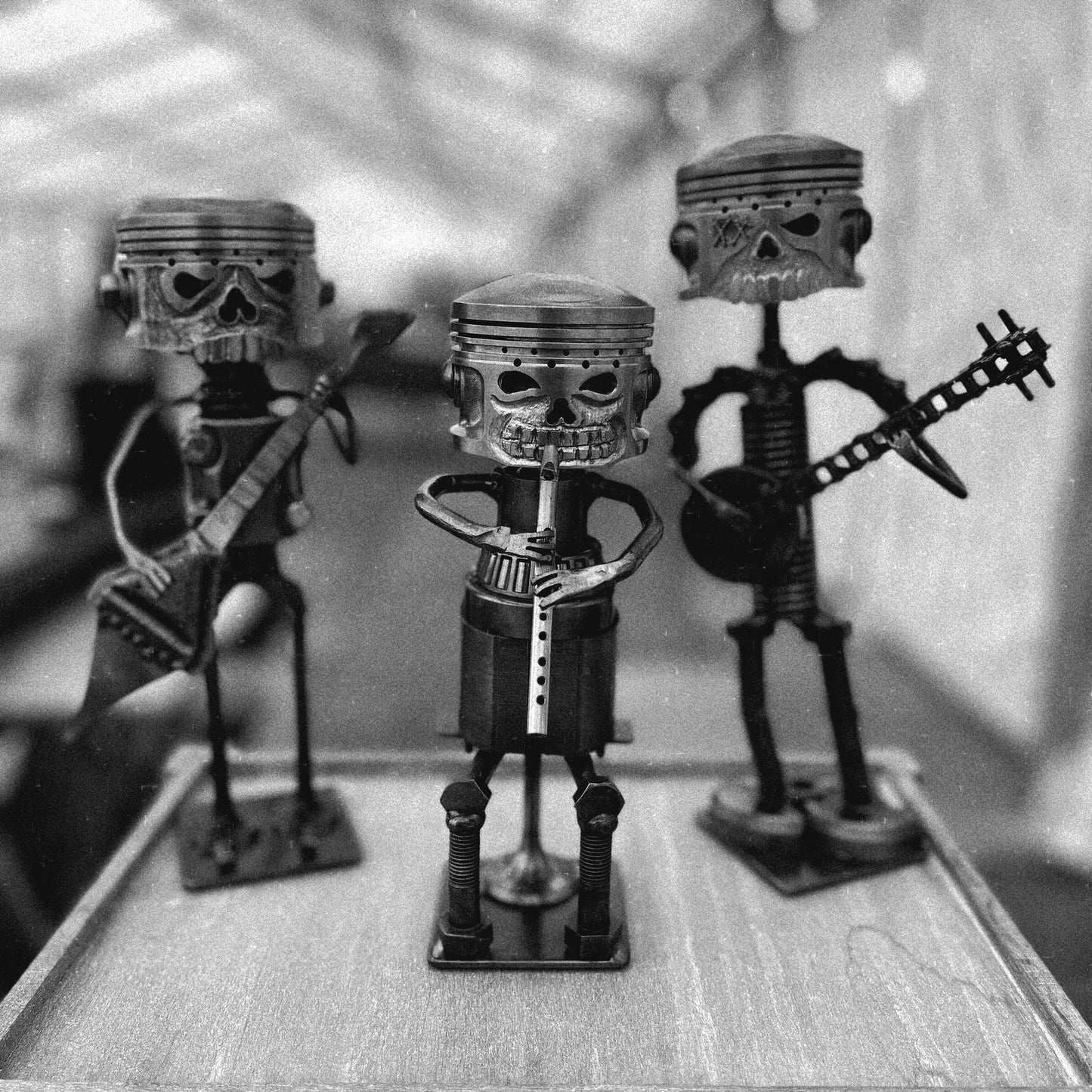 Trio of handmade metal musician sculptures crafted from recycled automotive parts including pistons, bolts, and spanners, displayed against a grey background — quirky scrap metal art band perfect for music lovers, steampunk collectors, or industrial decor.