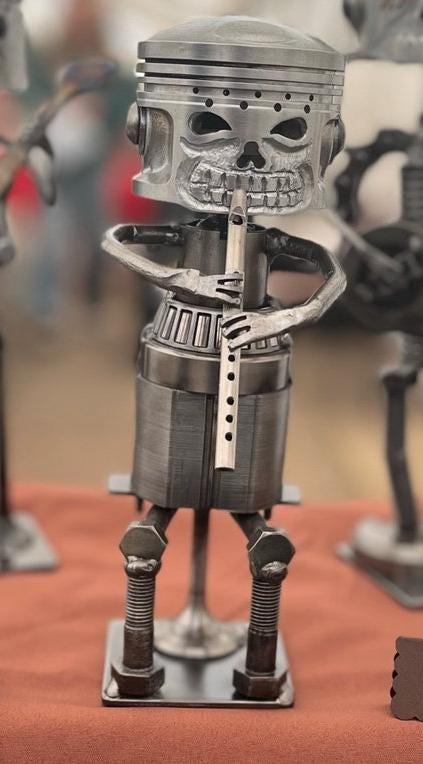 Upcycled metal tin whistle player sculpture with piston skull head, crafted from recycled motorbike parts — industrial-style music-themed home decor or musician gift.