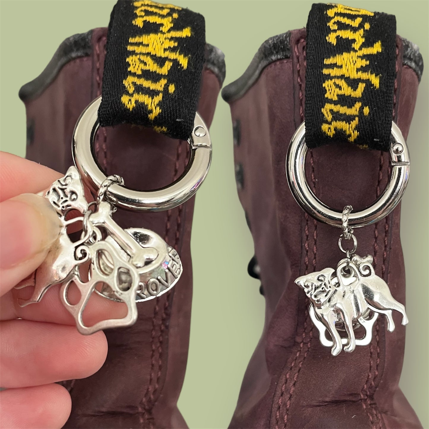 Close-up of handmade silver boot charms with pug dog, paw print, and dog bowl with bone designs clipped onto black boot tabs