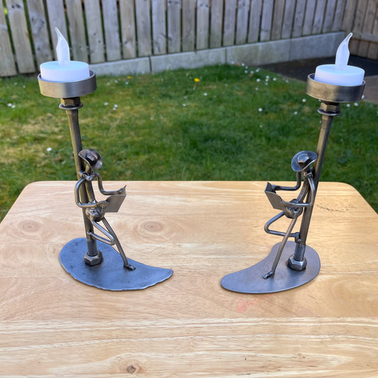Scrap metal sculpture of a man reading a newspaper while leaning against a lamp post, which doubles as a tealight holder. Handcrafted from upcycled nuts, nails, and other metal parts. Functional industrial art for home or office decor.