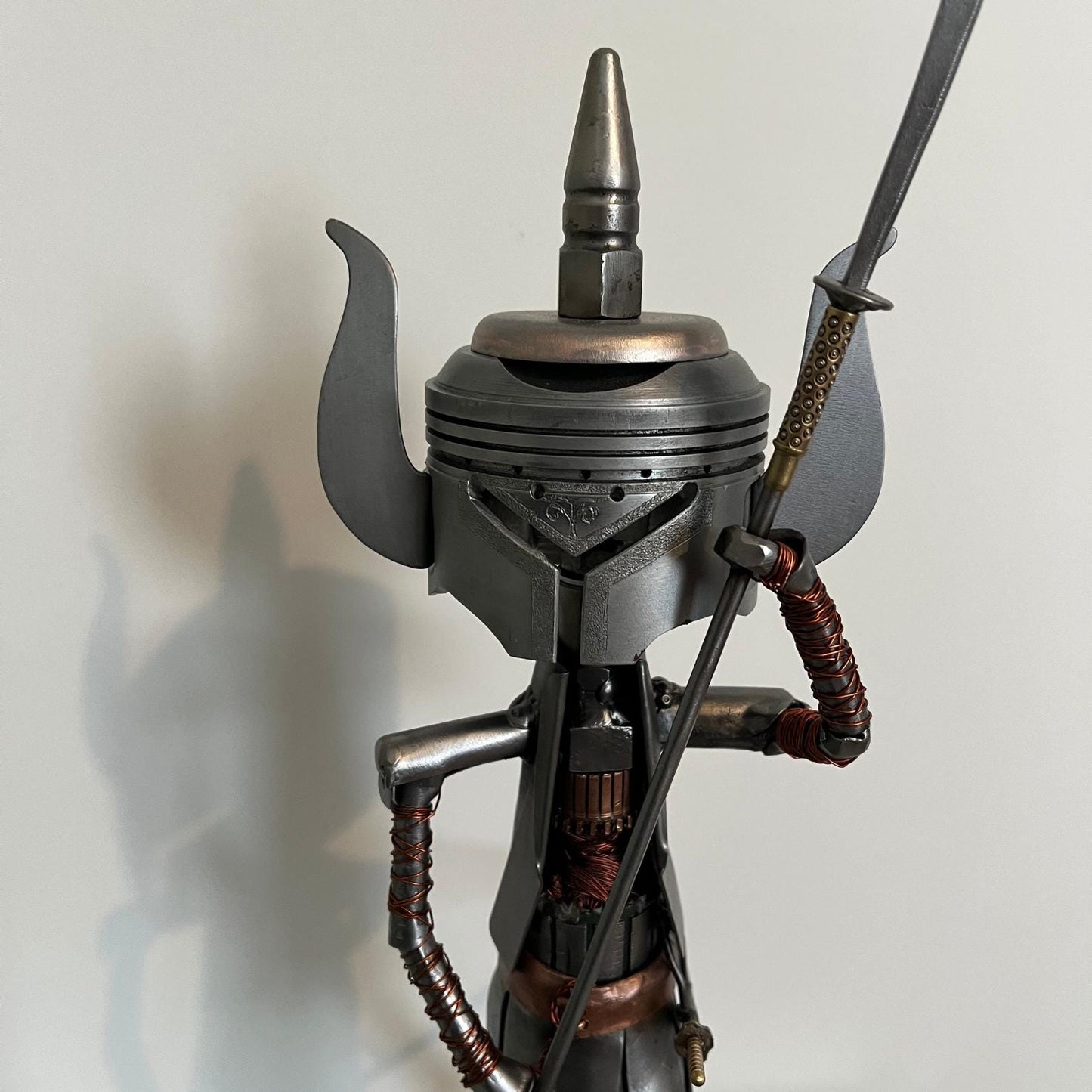 Samurai warrior sculpture made from a piston head, featuring copper and steel armor, a wooden base, and a sword. Close up of upper body.