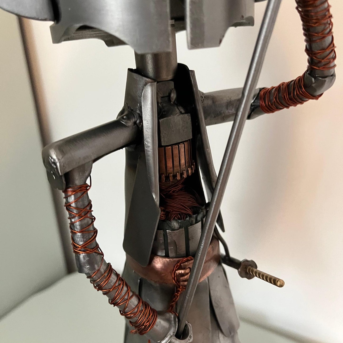 Samurai warrior sculpture made from a piston head, featuring copper and steel armor, a wooden base, and a sword. Close up of torso.