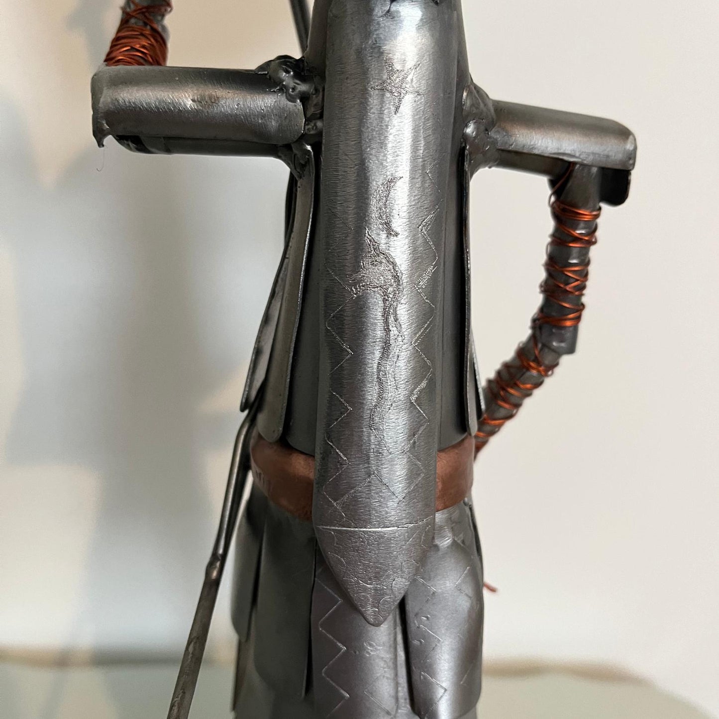 Samurai warrior sculpture made from a piston head, featuring copper and steel armor, a wooden base, and a sword. Close up of back.