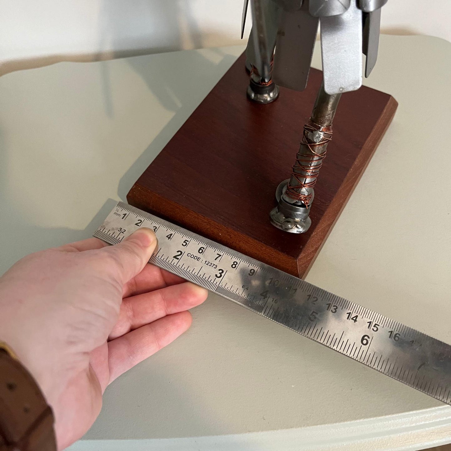 Samurai warrior sculpture made from a piston head, featuring copper and steel armor, a wooden base, and a sword. Showing width measurement of base.