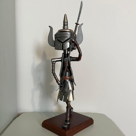 Samurai warrior sculpture made from a piston head, featuring copper and steel armor, a wooden base, and a sword. A unique blend of mechanical art and traditional Japanese warrior aesthetics.
