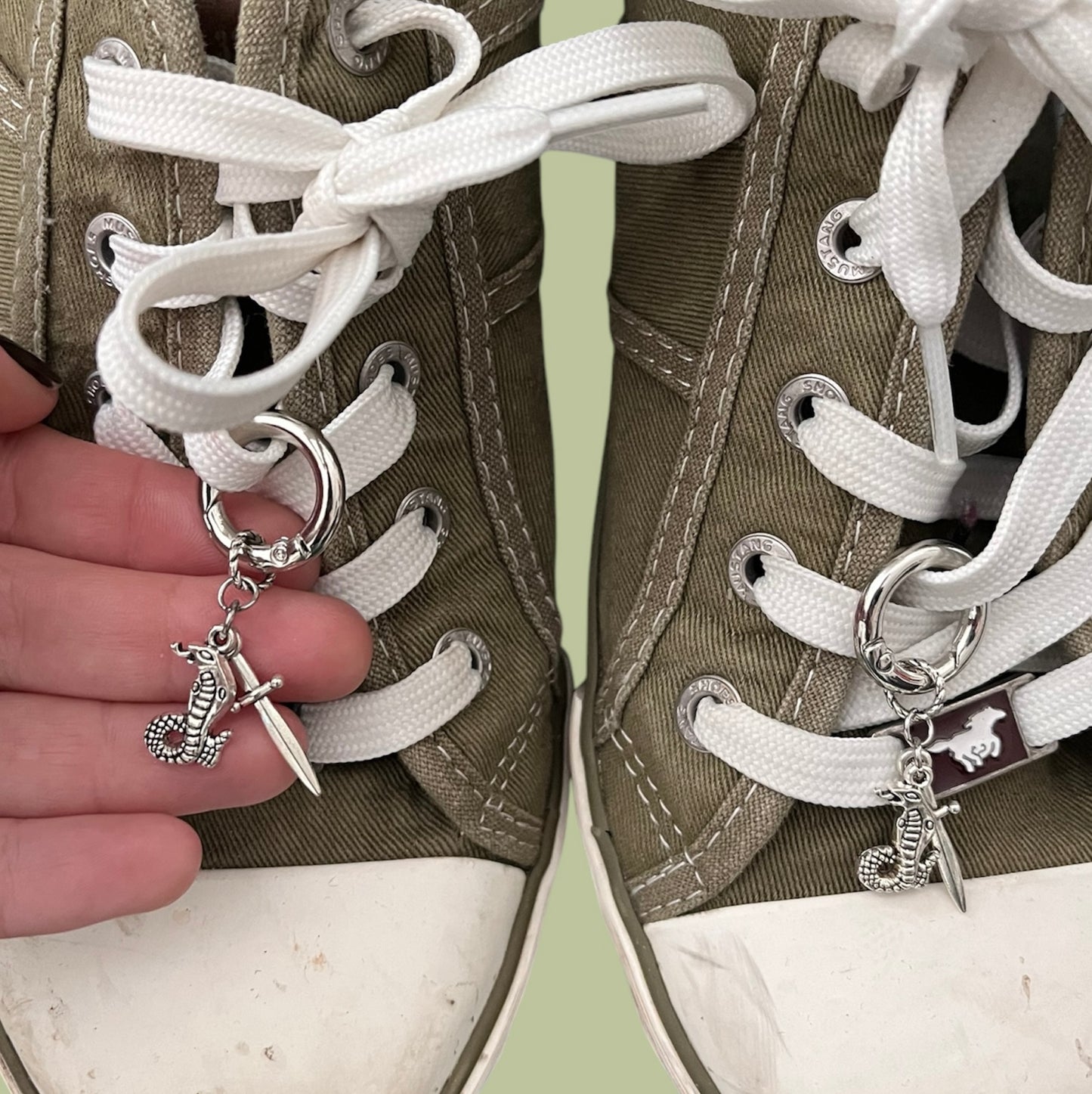 Close-up of handmade silver lace charms with cobra snake and sword designs clipped onto white shoelaces
