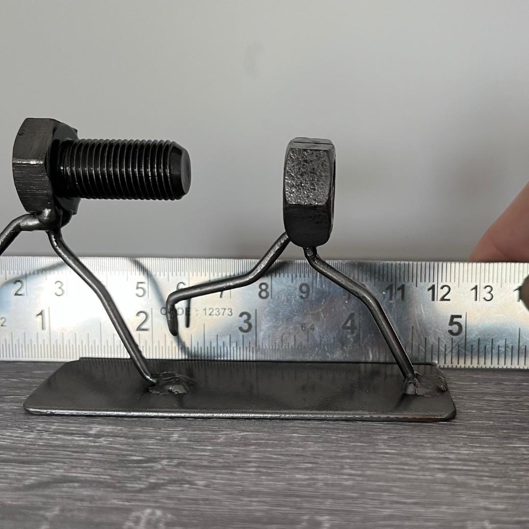 Whimsical sculpture of a bolt chasing a nut, symbolising the playful pursuit of connection. Ideal for tinkerers, engineers, and lovers of metal art and puns. Showing length measurement.