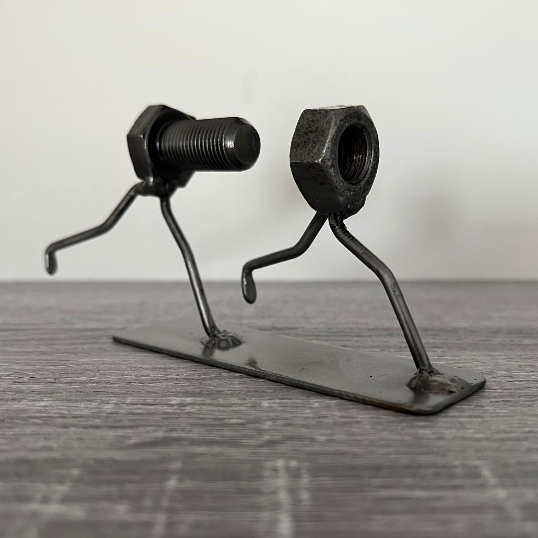 Whimsical sculpture of a bolt chasing a nut, symbolising the playful pursuit of connection. Ideal for tinkerers, engineers, and lovers of metal art and puns.