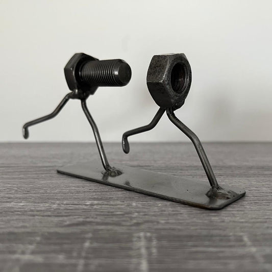Whimsical sculpture of a bolt chasing a nut, symbolising the playful pursuit of connection. Ideal for tinkerers, engineers, and lovers of metal art and puns.