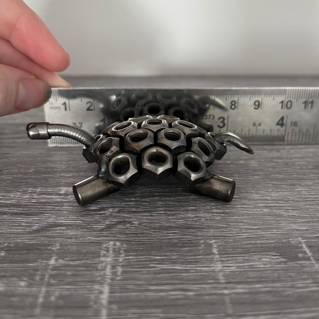 Industrial-style scrap metal tortoise sculpture made from hex nuts and bolts, handmade recycled metal art ornament on wood background, showing length