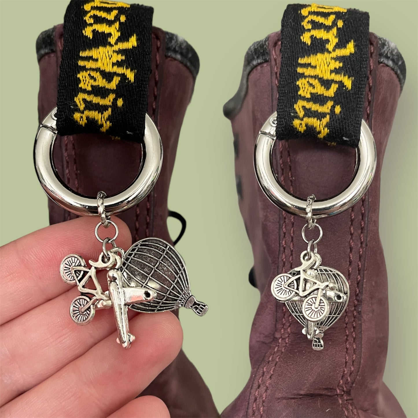Close-up of handmade silver boot charms with bicycle, aeroplane, and hot air balloon designs clipped onto black boot tabs