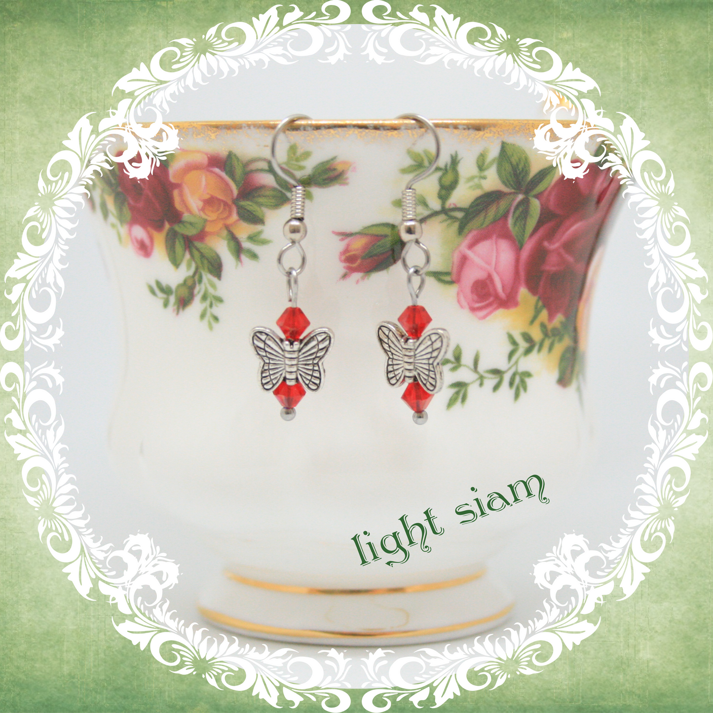 Handmade silver butterfly earrings with red crystal beads shown on floral china teacup