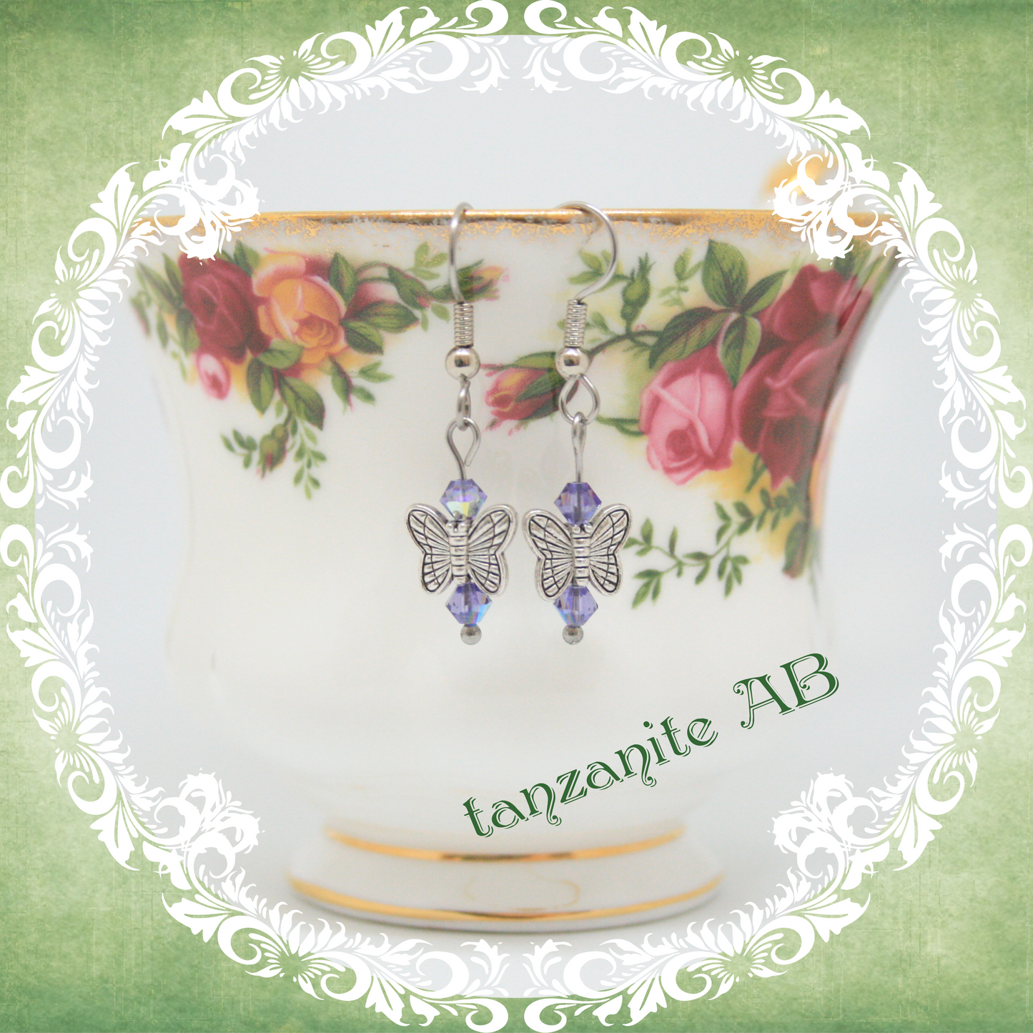 Handmade silver butterfly earrings with bluish purple crystal beads shown on floral china teacup