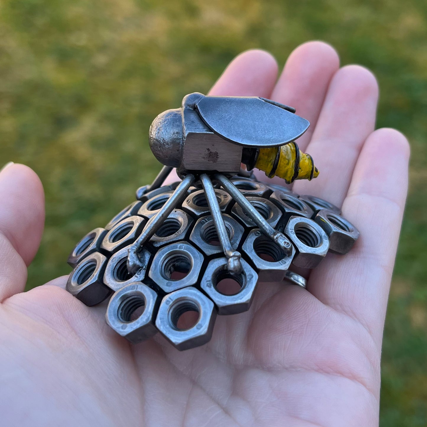 Handmade scrap metal bee sculpture with a screw body and hex nut honeycomb base, unique industrial decor or gift for bee lovers, held by a woman's hand.