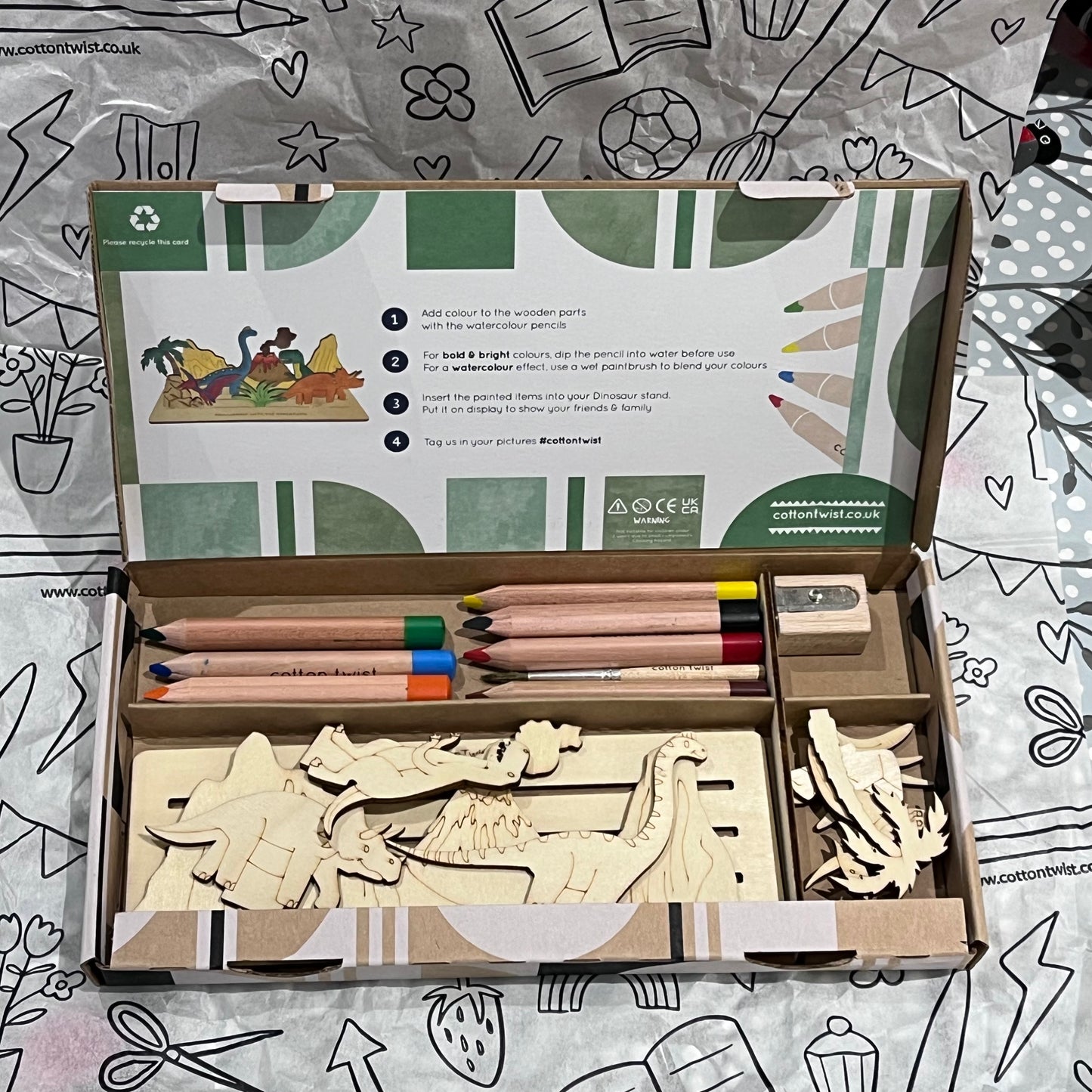 Plastic-free kids dinosaur craft kit with wooden dinosaur cutouts, watercolor pencils, brush, and stand, box open