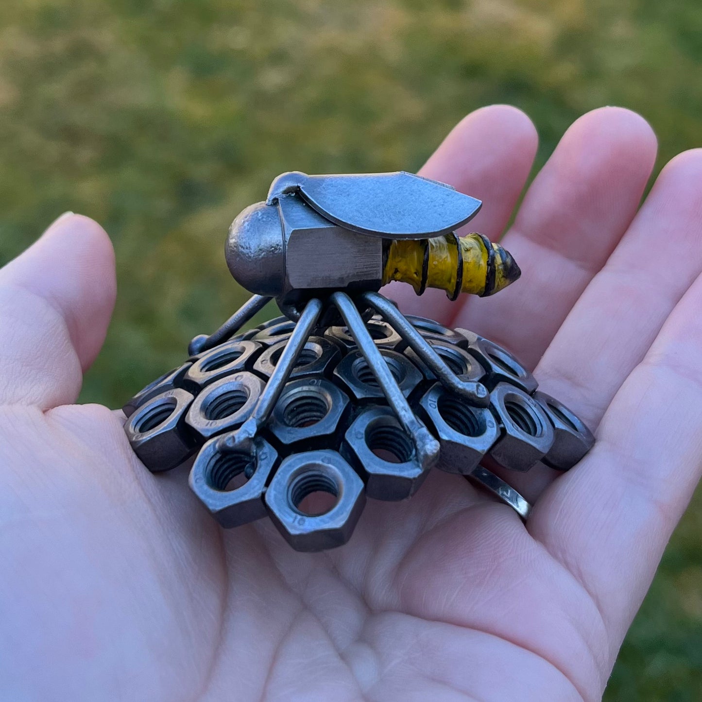 Handmade scrap metal bee sculpture with a screw body and hex nut honeycomb base, unique industrial decor or gift for bee lovers, held by a woman's hand.