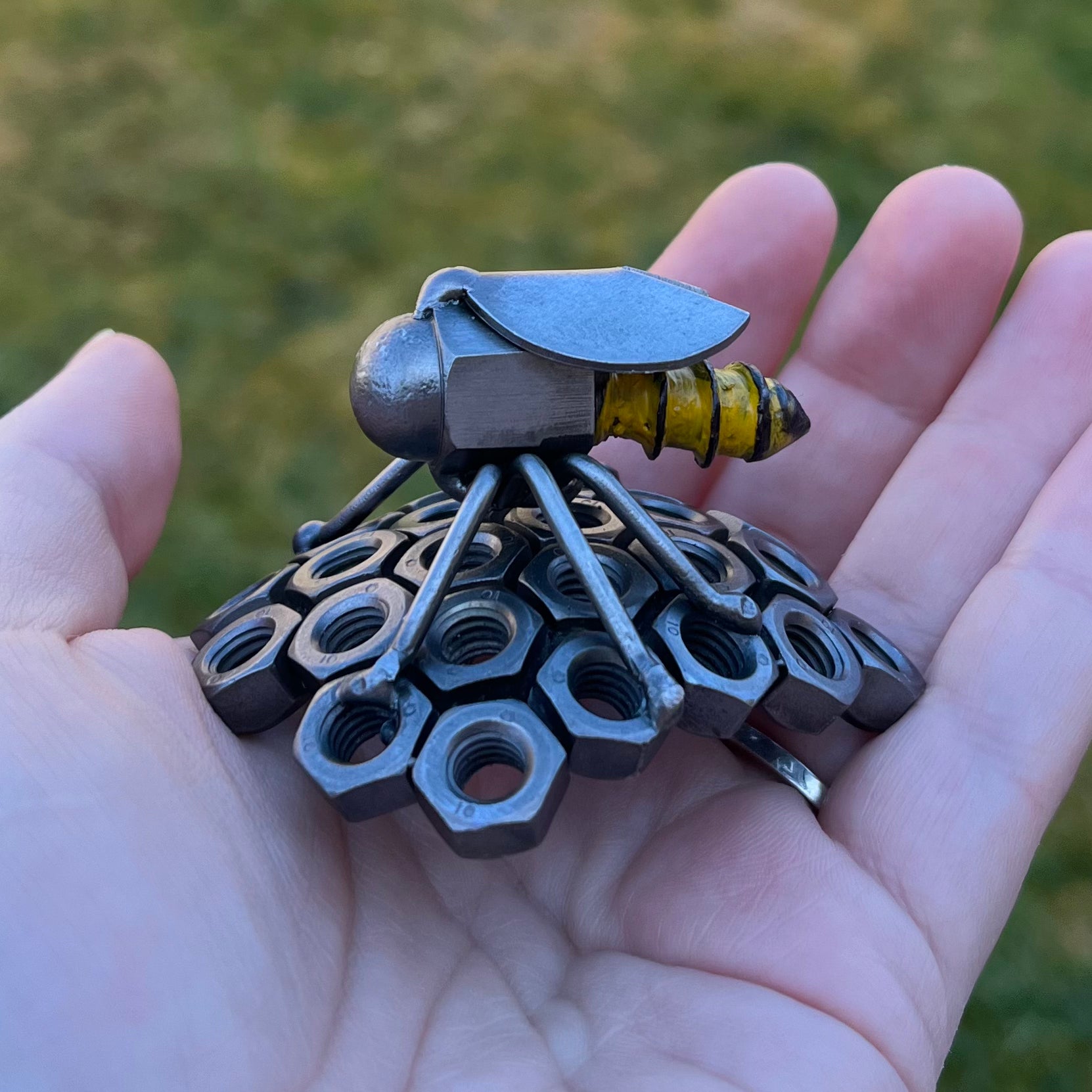 Handmade scrap metal bee sculpture with a screw body and hex nut honeycomb base, unique industrial decor or gift for bee lovers, held by a woman's hand.