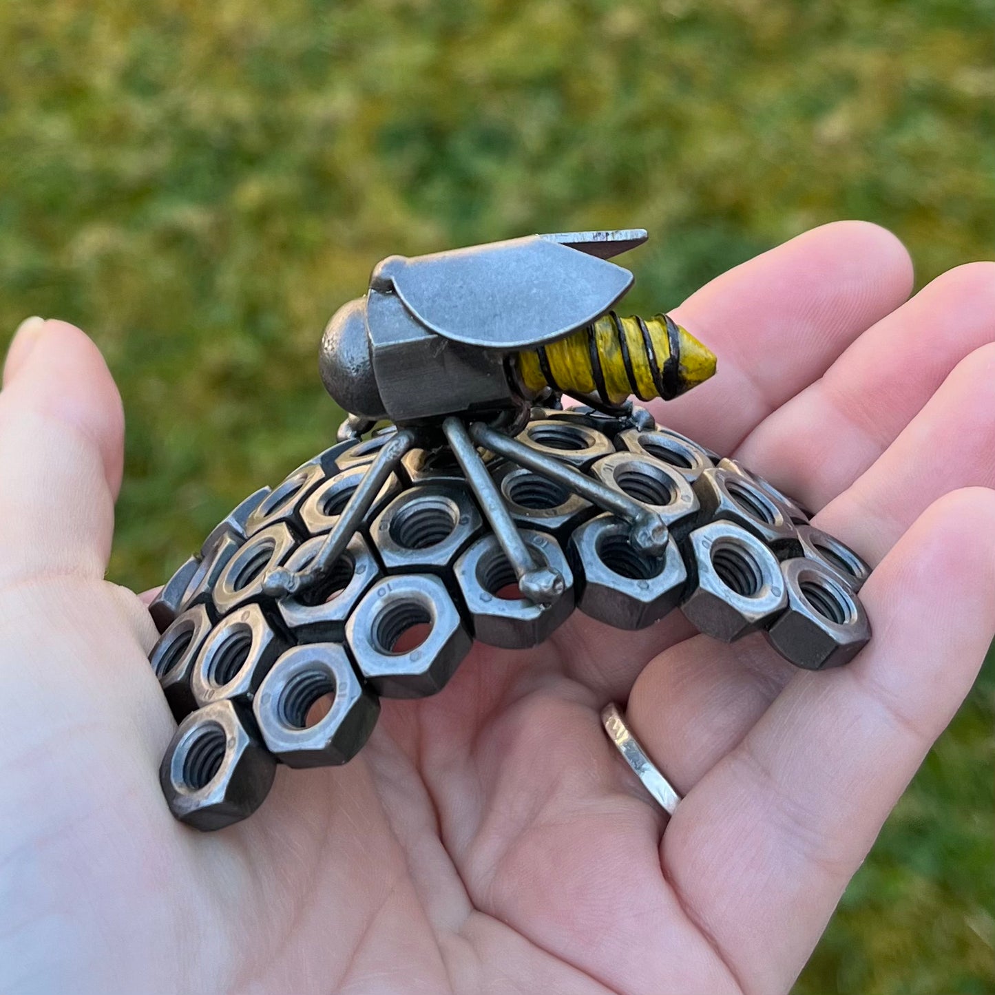 Handmade scrap metal bee sculpture with a screw body and hex nut honeycomb base, unique industrial decor or gift for bee lovers, held by a woman's hand.