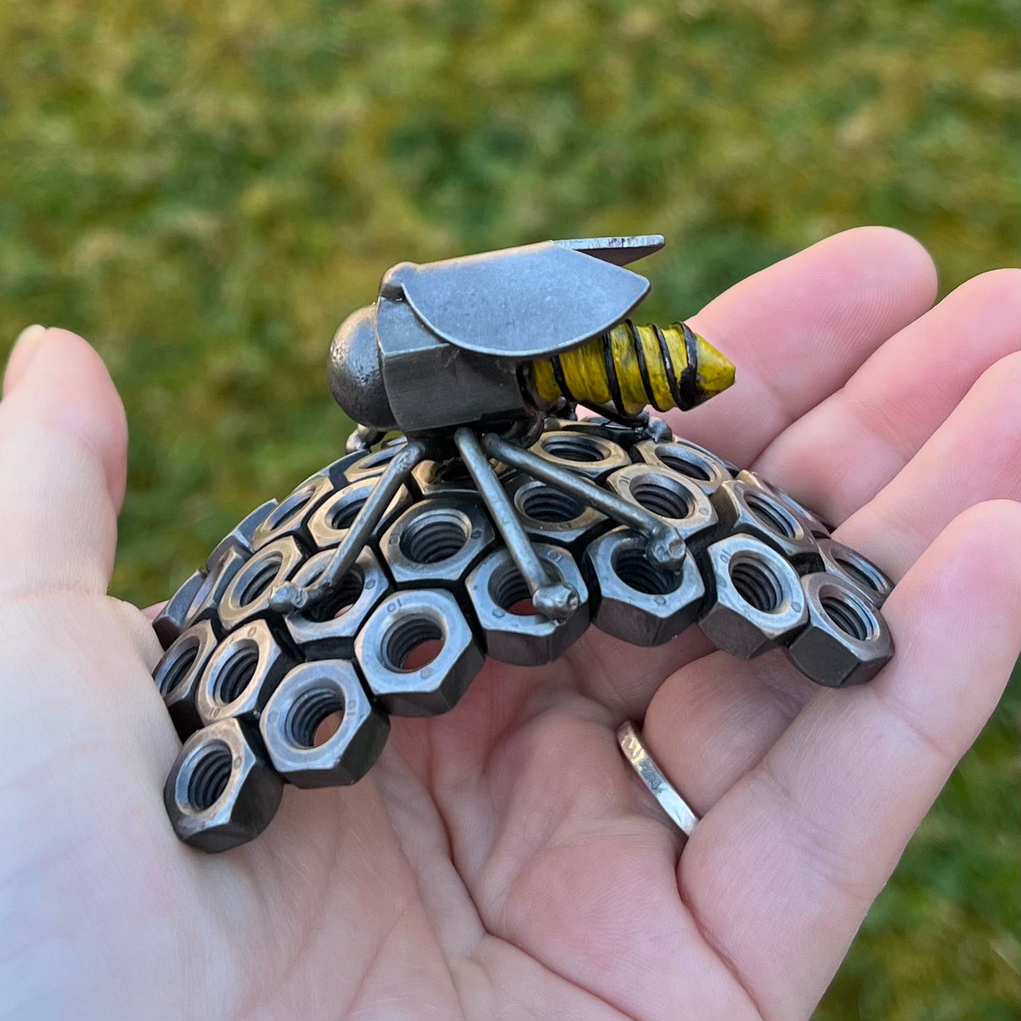 Handmade scrap metal bee sculpture with a screw body and hex nut honeycomb base, unique industrial decor or gift for bee lovers, held by a woman's hand.