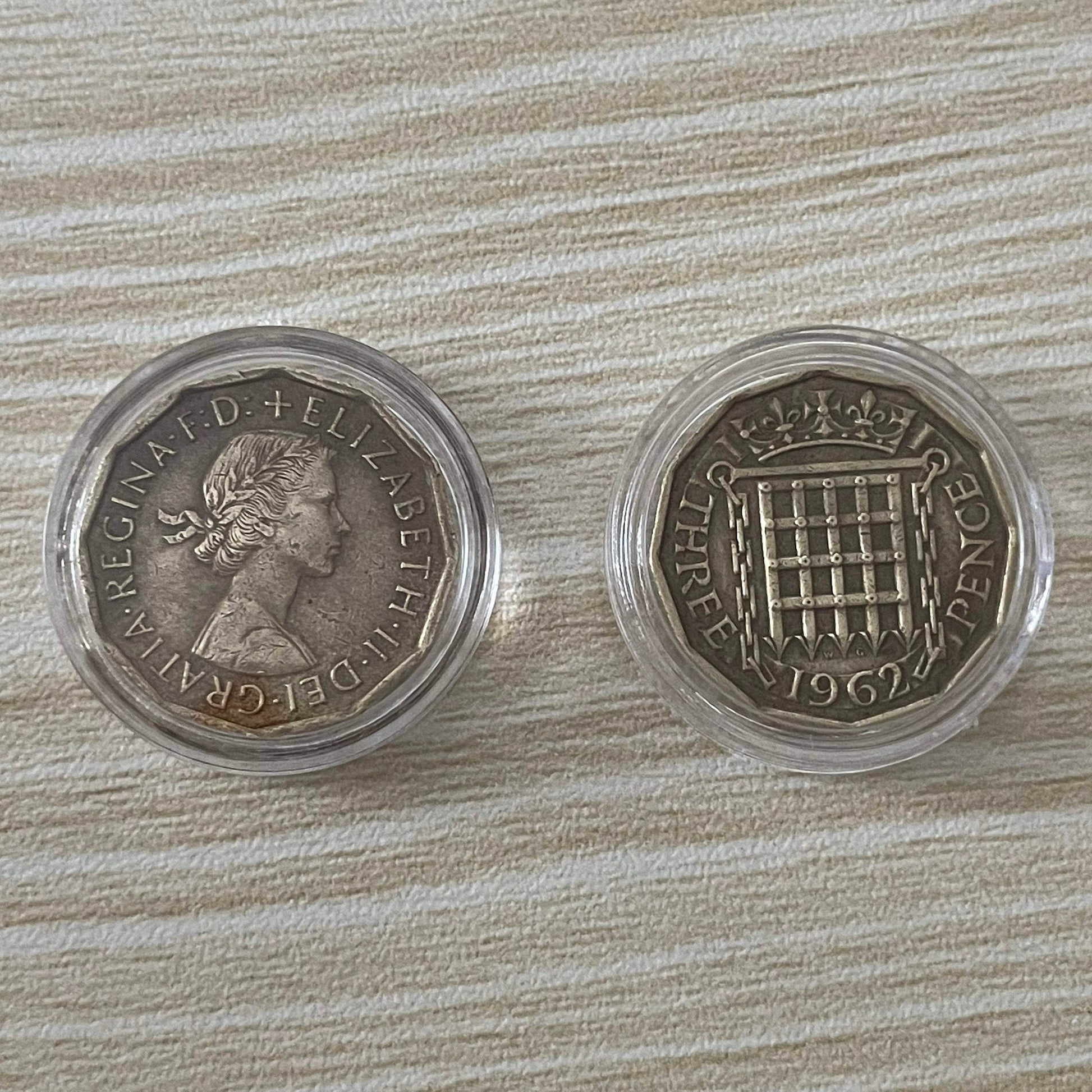 Queen Elizabeth II brass threepence coins in protective capsules, obverse and reverse
